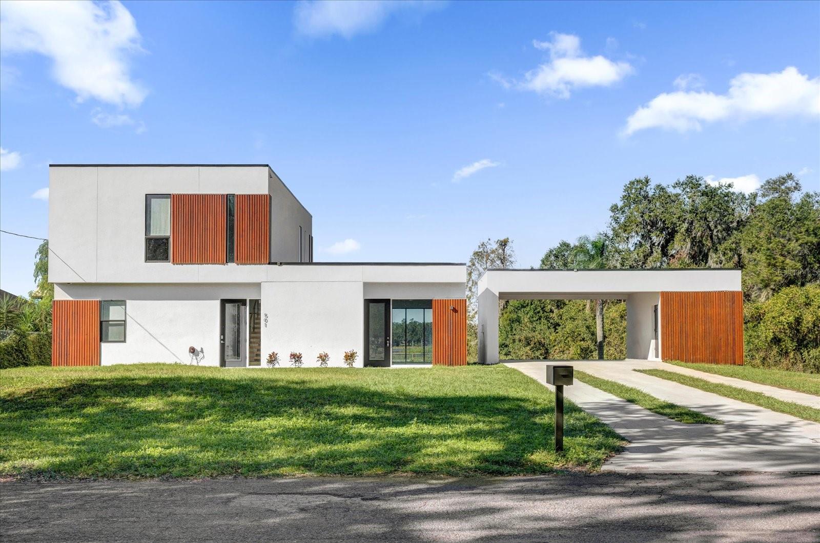 Step into this extraordinary two-story residence, where German modern architecture meets contemporary elegance. The striking façade instantly captivates with its harmonious blend of glass and wood, creating a warm and inviting entry. As you enter, you’re greeted by an expansive open floor plan that seamlessly merges indoor and outdoor living. Architectural sophistication flows throughout the home, highlighted by an abundance of glass and rich wooden accents. A spectacular floating staircase elegantly divides the foyer from the main entertainment spaces, adding a touch of artistry to the entrance. The heart of the home is a luxurious, sunlit kitchen, featuring a stylish island and an abundance of storage with sleek European-style cabinets and a spacious pantry. It overlooks the dining area, offering breathtaking views of the serene lake, perfect for hosting gatherings or quiet family dinners. On the first floor, a comfortable bedroom with a full bathroom provides convenience for guests or family. Also, you’ll find a delightful living room awash in natural light, accentuated by three sets of sliding glass doors that open to a private outdoor oasis—ideal for leisurely afternoons or entertaining under the stars. Ascending the staircase, Retreat to the owner's suite situated at the back of the home, where sweeping water views greet you from your private balcony. The expansive owner’s bathroom is a spa-like escape, boasting dual vanities, a glass-enclosed shower, and a generous walk-in closet. Nestled on a prime corner lot between a picturesque channel and the stunning lake, this home offers the ultimate resort-style outdoor living experience. Additional highlights include a spacious covered porch and a two-car garage, rounding out this remarkable property designed for both comfort and luxury. Experience the perfect blend of modern design and tranquil living—your dream home awaits!