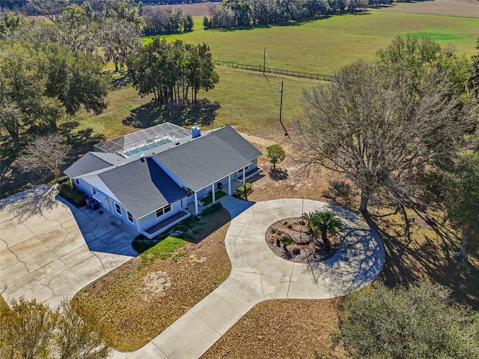 Welcome to your private retreat—a custom concrete block estate offering six bedrooms and three bathrooms, gracefully positioned on 10 breathtaking acres of mature oaks. Fully fenced and gated, this exceptional single-parcel property delivers ultimate privacy and peace of mind while remaining conveniently close to town. A serene, tree-lined drive sets the tone as you approach, opening to a circular driveway and a welcoming front porch that invites you to slow down and stay awhile. Inside, the thoughtfully designed floor plan blends elegance with everyday functionality. A formal dining room provides the perfect setting for gatherings, while a dedicated piano room or home office offers flexibility to fit your lifestyle. The spacious primary suite is a true sanctuary, featuring two walk-in closets, dual vanities, a jetted soaking tub, and private access to the screened pool patio—creating a seamless indoor-outdoor escape. On the opposite wing, five generously sized bedrooms are filled with natural light and offer comfort and space for family and guests. The kitchen is designed for both daily living and entertaining, complete with abundant cabinetry and a casual seating area for relaxed meals and conversation. In the living room, expansive glass sliders disappear into the wall, opening fully to the oversized screened-in pool patio and transforming the space into a grand open-air entertaining area you’ll enjoy year-round. A dedicated pool bath with direct patio access adds convenience for guests.
Perched atop a scenic hill overlooking rolling countryside, this property offers true country living with no HOA or deed restrictions. Additional features include a laundry room with exterior access—ideal as a mudroom, a dedicated storage room, and a spacious 30x50 detached concrete garage with ample room for equipment, recreational vehicles, tools, and hobbies. An RV hookup and additional septic tank add even more versatility. The seller has completed extensive improvements, including enclosing the garage to create two spacious bedrooms, fresh interior and exterior paint, new hardwood flooring and carpet, updated trim, a new dishwasher, new light fixtures, and a newly screened pool enclosure—ensuring the home is move-in ready. Despite its private, secluded, and peaceful setting, the property is just minutes from Alachua, High Springs, Gainesville, and Jonesville, with convenient access to the University of Florida, Santa Fe College, UF Health Shands Hospital, and HCA Florida North Florida Hospital. This one-of-a-kind estate beautifully combines space, comfort, and accessibility. Private. Secluded. Quiet—yet close to everything. A must-see property that truly captures the best of North Florida living.