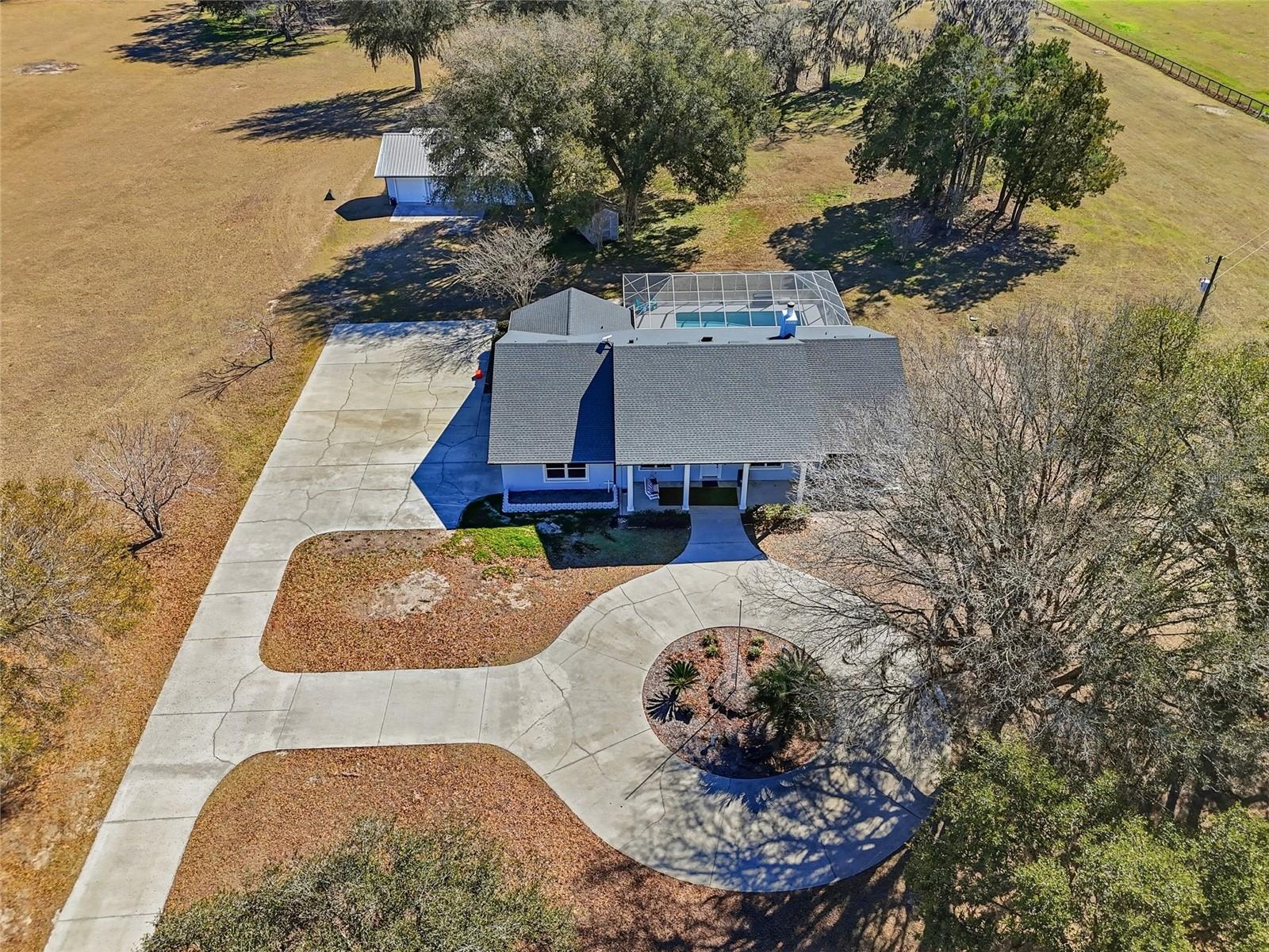 Welcome to your private retreat—a custom concrete block estate offering six bedrooms and three bathrooms, gracefully positioned on 10 breathtaking acres of mature oaks. Fully fenced and gated, this exceptional single-parcel property delivers ultimate privacy and peace of mind while remaining conveniently close to town. A serene, tree-lined drive sets the tone as you approach, opening to a circular driveway and a welcoming front porch that invites you to slow down and stay awhile. Inside, the thoughtfully designed floor plan blends elegance with everyday functionality. A formal dining room provides the perfect setting for gatherings, while a dedicated piano room or home office offers flexibility to fit your lifestyle. The spacious primary suite is a true sanctuary, featuring two walk-in closets, dual vanities, a jetted soaking tub, and private access to the screened pool patio—creating a seamless indoor-outdoor escape. On the opposite wing, five generously sized bedrooms are filled with natural light and offer comfort and space for family and guests. The kitchen is designed for both daily living and entertaining, complete with abundant cabinetry and a casual seating area for relaxed meals and conversation. In the living room, expansive glass sliders disappear into the wall, opening fully to the oversized screened-in pool patio and transforming the space into a grand open-air entertaining area you’ll enjoy year-round. A dedicated pool bath with direct patio access adds convenience for guests.
Perched atop a scenic hill overlooking rolling countryside, this property offers true country living with no HOA or deed restrictions. Additional features include a laundry room with exterior access—ideal as a mudroom, a dedicated storage room, and a spacious 30x50 detached concrete garage with ample room for equipment, recreational vehicles, tools, and hobbies. An RV hookup and additional septic tank add even more versatility. The seller has completed extensive improvements, including enclosing the garage to create two spacious bedrooms, fresh interior and exterior paint, new hardwood flooring and carpet, updated trim, a new dishwasher, new light fixtures, and a newly screened pool enclosure—ensuring the home is move-in ready. Despite its private, secluded, and peaceful setting, the property is just minutes from Alachua, High Springs, Gainesville, and Jonesville, with convenient access to the University of Florida, Santa Fe College, UF Health Shands Hospital, and HCA Florida North Florida Hospital. This one-of-a-kind estate beautifully combines space, comfort, and accessibility. Private. Secluded. Quiet—yet close to everything. A must-see property that truly captures the best of North Florida living.
