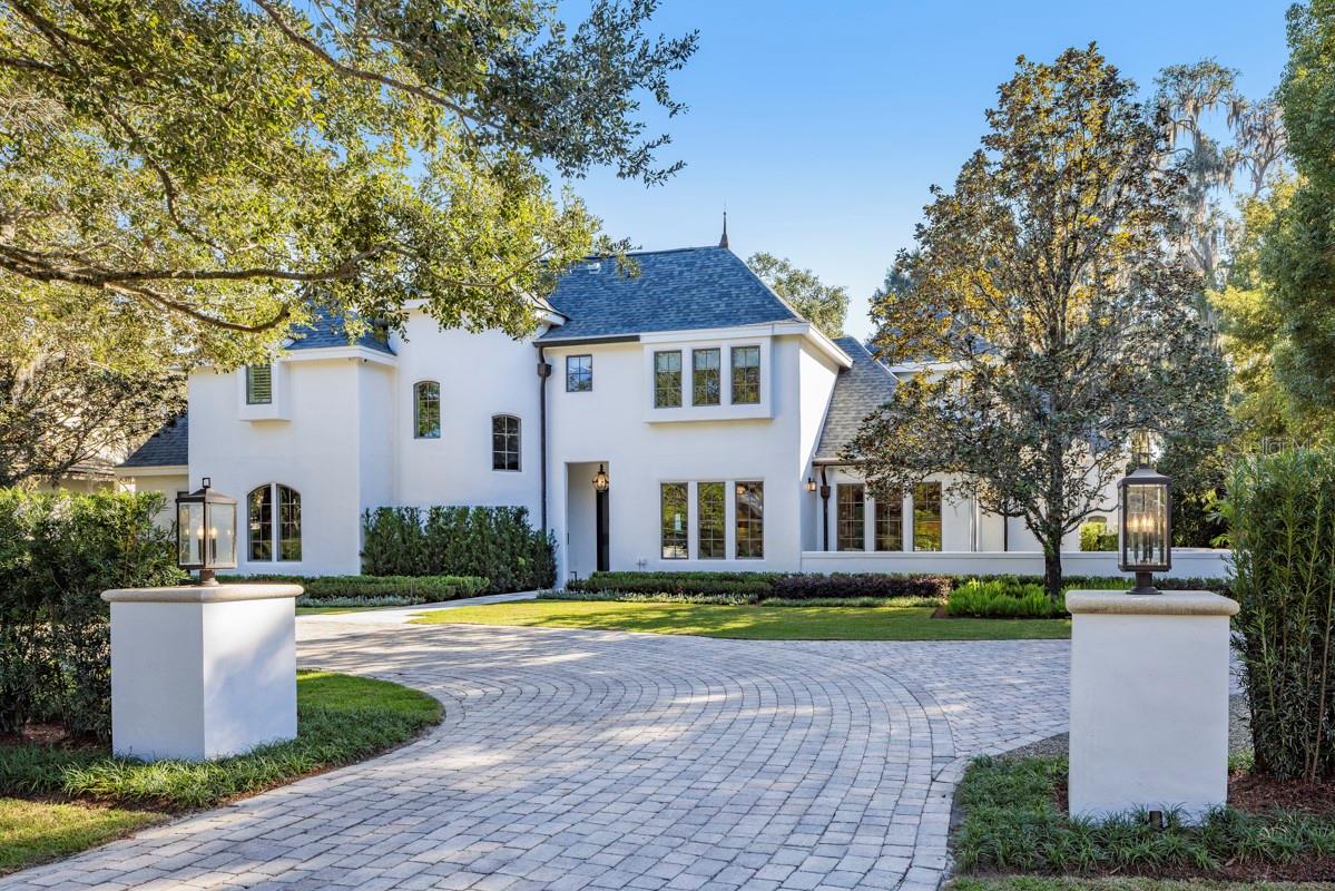 Along one of the cobblestone brick streets in the prestigious Via’s of Winter Park, this completely renovated residence pairs timeless European influence with clean architectural lines and bespoke finishes throughout. A circular driveway and manicured grounds designed by Signature Landscapes create a graceful approach. Inside, a dramatic curved staircase crowned by a breathtaking 1960s vintage Venini chandelier immediately sets the tone for the exceptional craftsmanship carried throughout the home. The main gathering room is striking and inviting, defined by vaulted ceilings, a Sequoia leathered stone fireplace hearth, and a wall of glass sliders that open seamlessly to the covered lanai and heated saltwater pool. The connection between indoors and out is effortless, designed for year-round entertaining and relaxed daily living, enhanced by a full outdoor audio system. A light-filled breakfast room sits just off the kitchen, offering an intimate everyday dining space. At the heart of the home, the custom kitchen is a showpiece. Naica leathered stone countertops and a waterfall island are complemented by custom cabinetry extending to the ceiling, a professional-grade appliance suite featuring Sub-Zero and Wolf, and convenience of two Miele dishwashers. Directly adjacent, the pantry mirrors the kitchen’s cabinetry and craftsmanship and features a built-in coffee station, seamlessly connecting to the laundry area and three-car side-entry garage. A beautifully appointed guest powder room with an integrated sink is thoughtfully positioned nearby. A separate lounge showcases a custom wet bar highlighted by dramatic stonework and an integrated sink, an elegant setting for conversation and evening gatherings. A dedicated office positioned just outside the primary suite features a wall of floor-to-ceiling shelving, cabinetry and file drawers. The primary suite serves as a private sanctuary, enhanced by vaulted ceilings, backyard views and a stately two-sided stone fireplace shared with the office. Two custom walk-in closets provide exceptional storage, while the spa-inspired bath showcases Taj Mahal leathered stone countertops with integrated dual sinks, a soaking tub and an oversized glass shower with dual showerheads. Upstairs, four additional bedrooms with custom closets are complemented by beautifully finished baths and a loft sitting area with hallway built-ins. Two of the bedrooms and a bath may be closed off to create a private suite, ideal for guests or multigenerational living. A secondary staircase leads to an impressive media room equipped with a 98-inch television, state-of-the-art 7.1 surround sound and extensive storage. Outdoor living is equally elevated, featuring a weathered marble pool deck, dedicated pool bath, newly installed summer kitchen with Coyote gas grill, hood vent, sink, and leathered stone counters and backsplash, plus an outdoor living room anchored by a two-sided fireplace and television. Modern systems include a Lutron lighting system on the main level, water filtration & softener, ADT alarm - security cameras throughout and a whole-home natural gas generator. Every element of this residence has been newly installed and custom-designed, resulting in a home that blends sophisticated design, advanced functionality, and exceptional spaces for intimate living and grand entertaining. From custom millwork to curated stone selections, this home reflects uncompromising quality and thoughtful design.