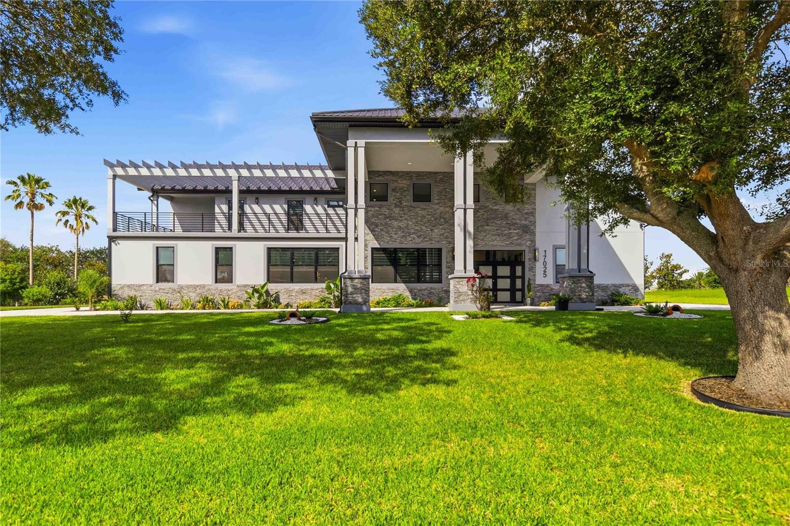Price Reduced! Why wait to build when something better already exists? The moment you step through the front door, the question answers itself. A soaring double-height great room commands your full attention — dramatic chandelier overhead, floating staircase with glass railings rising alongside you, walls of windows pulling the Florida landscape into every sightline. This is not a home that slowly reveals itself. It arrives all at once. Set within an exclusive gated community with coveted Chain of Lakes access, this not even one-year-old custom contemporary estate spans just over 7,000 square feet of flawlessly executed living space — designed from the ground up with the kind of intention that simply cannot be replicated at any price point. The chef’s kitchen is a study in contrast and refinement: matte black flat-panel cabinetry trimmed in warm wood slat detail, a waterfall-edge Calacatta marble island, brushed gold fixtures, Café appliances, and a globe pendant chandelier anchoring the adjacent formal dining space. Every surface, every material, every proportion was considered.The primary suite is its own world. Positioned privately on the upper level, it unfolds with wide-plank hardwood flooring, a custom designer accent wall, and a spa bath that belongs in an architectural publication — floor-to-ceiling Calacatta marble enveloping a freestanding soaking tub, frameless glass shower with a built-in bench, and brushed gold fixtures at every turn. A dedicated ensuite laundry room connects seamlessly to the main living areas, while a private lounge and a flex room ideal for a home office or workout studio round out the suite. This is not just a primary bedroom — it is a private residence within the estate, designed for those who understand that true luxury is the freedom to never leave your own floor.Additional bedrooms are equally considered. Each is generously sized with its own ensuite bath and an oversized walk-in closet — thoughtfully laid out for family members and guests alike to enjoy genuine privacy and comfort. A dedicated home theater with tiered recliner seating and a separate media room add yet another layer of intentional living, along with storage throughout that is simply unexpected at every turn.The outdoor living experience rivals anything indoors. A vaulted covered lanai finished with a dramatic floor-to-ceiling stone accent wall opens to a full outdoor kitchen and fire pit lounge, all screened and climate-softened with automatic retractable screens. Beyond, a resort-style pool with swim shelf sit beneath a grand screen enclosure — wide travertine surround, lush tropical landscaping, and a permanently open backdrop of serene green parkland. No rear neighbors now. No rear neighbors ever. The fully self-contained guest suite is an estate within the estate — its own full kitchen, living and dining area, in-unit washer and dryer, and private entrance. Ideal for multigenerational living, extended guests, or income-producing opportunity without compromise .All appliances convey. Furnishings available by separate negotiation for a seamless turnkey transition. Forty-five minutes from Orlando International Airport, Walt Disney World, and Central Florida’s premier entertainment corridor. Immediate access to Florida’s Turnpike and Highway 47. A community boat ramp, fishing pier, and covered dock place the full Chain of Lakes at your doorstep. One-of-a-kind.