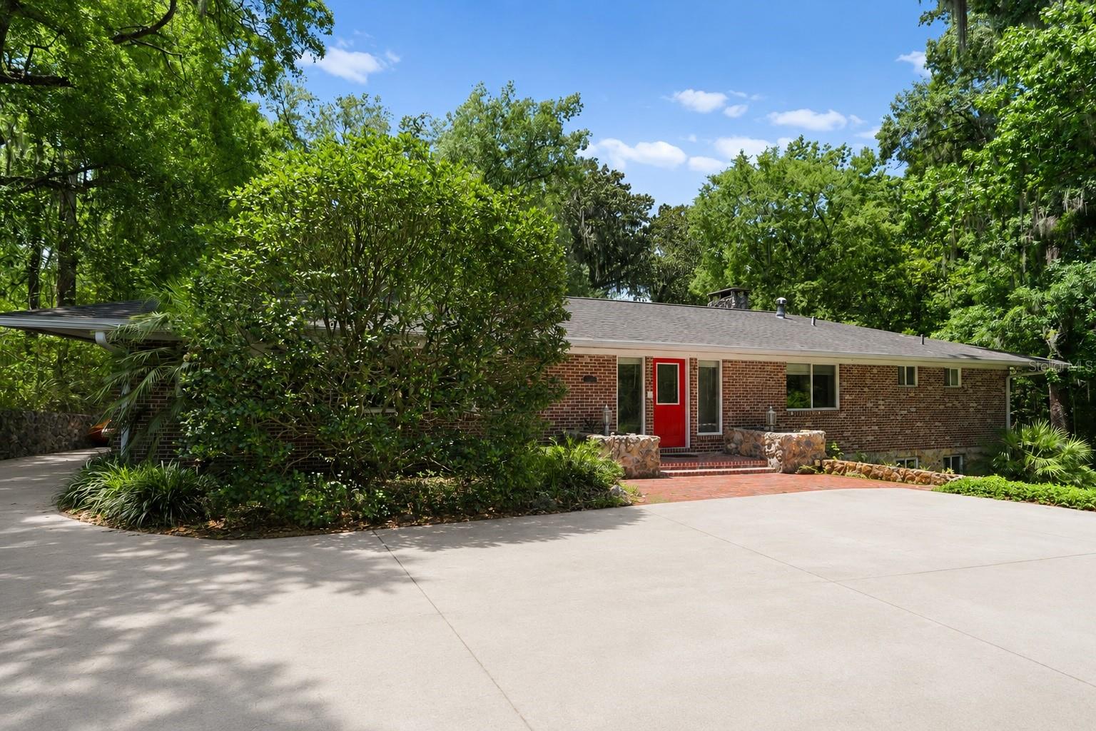 Overlooking a peaceful creek and tucked behind a fully fenced yard, this expansive brick ranch delivers a rare combination of privacy, flexibility, and resort-style outdoor living — all in one of Gainesville's most convenient locations. At the heart of the home, an open-concept living area anchored by a dramatic stone fireplace flows naturally into the dining room and updated kitchen. The kitchen features generous prep space, stainless steel appliances, and a gas range — ideal for everyday living and effortless entertaining. Oversized sliding glass doors line the rear of the home, flooding the interior with natural light and opening directly onto an expansive deck overlooking the pool and a canopy of mature trees. The backyard is a true retreat. A sparkling pool, multiple lounging and dining areas, an outdoor kitchen, basketball area, and lush creekside setting create an outdoor experience that feels private, tranquil, and resort-caliber — perfect for large gatherings or quiet evenings in nature. The main residence offers four upstairs bedrooms, including one with a spiral staircase leading to a private downstairs room and full bath with exterior access — a setup that adapts beautifully to a home office, studio, teen suite, or guest quarters. An attached in-law suite with its own kitchen, private bath, and separate exterior entrance facing the pool adds exceptional versatility — ideal for multigenerational living, long-term guests, or rental income potential. Expansive windows frame wooded and creekside views from nearly every room, while the thoughtful layout balances open, communal spaces with comfortable privacy throughout. Ample parking and an attached two-car carport complete this one-of-a-kind property.