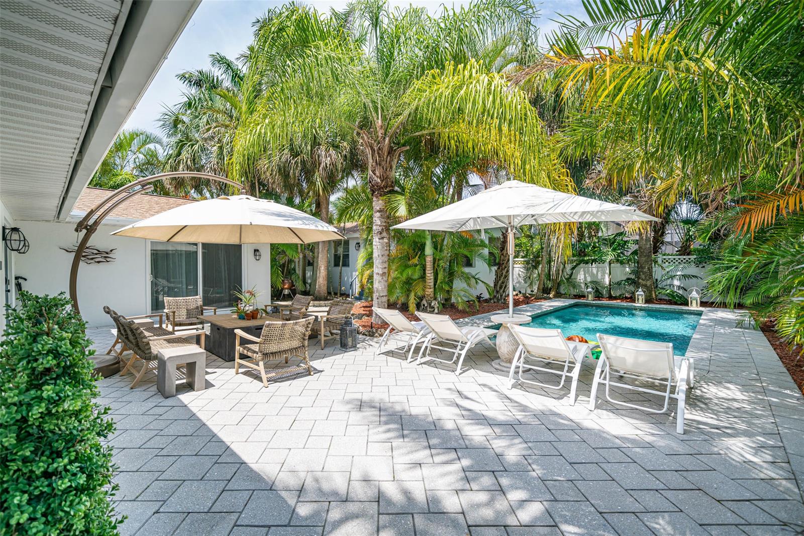 Here is your New Smyrna Beachside jewel with a GUEST HOUSE AND A SALT WATER POOL! Main home is 1671 sq ft. 3 bedroom/2.5 bath, and the guest house is 512 sq. ft. 1 bed/1 bath with an open bedroom style, full bath, full kitchen, and storage closet. Great for the in-laws, guests and working from home...at the beach!! The landscaping is absolutely incredible on this property! Lots of privacy and shade from mature palm trees, with brand new May 2021 LED landscape lighting in the front yard. The salt water pool pump was replaced and the interior resurfaced in 2017 with Pebble Tec. Surrounded by over 600 square feet of high end Artistic pavers featuring real seashells embedded in the tiles, this is a setting like you are in a resort and it's ready for your ultimate relaxation while enjoying your coffee or a cocktail! The inside of this home is just as amazing. Beautiful zero grout line neutral travertine tile throughout the main living areas, natural wood cabinets with stainless steel appliances, and attractive hood vent over the peninsula stove. The kitchen opens to your guests as you entertain at the bar that seats up to 8 and the dining area that seats 8. There is access to the back patio through the double doors directly off the kitchen so you can dine alfresco by the pool. Down one hallway are 3 bedrooms and 1.5 bathrooms; through another is a full bathroom and indoor laundry room leading to a spectacular great room with lots of windows showing off the exotic palm trees as natural light shines; vaulted ceilings and an 8ft. sliding glass door again leads to the pool area. Treat yourself to beach life in this great location on a quiet street and only a couple blocks to the no drive beach! The entire property is surrounded by vinyl fencing with 2 gates. Additional updates include the main home HVAC units replaced in 2020; large unit is sprayed with an anti corrosive coating. Guest house mini split replaced in 2017. Main home and guest house roof replaced in 2018. ;Water: City