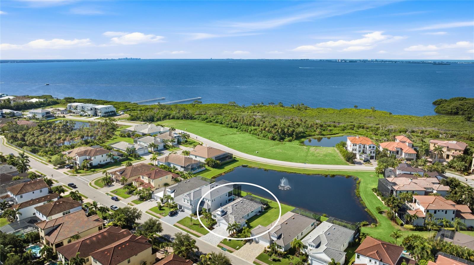 Welcome to Legends Bay, a gated enclave on Sarasota Bay where a private community path and pier lead to the water, Anna Maria Island's beaches are just minutes from your door, and IMG Academy is only moments away. For families drawn to the area by the academy, few neighborhoods put you this close to campus, turning early practices, matches, and everyday drop offs into a quick trip rather than a commute. Positioned on one of the neighborhood's premier waterfront homesites, this turnkey furnished three bedroom plus office residence delivers the full Gulf Coast package, water views, resort style outdoor living, and the confidence of newer construction. A tile roof, paver driveway, three car garage, and a cupola topped coastal contemporary facade create immediate curb appeal. Storm season brings peace of mind here rather than worry. A whole home generator, impact windows and doors, hurricane roof straps, and energy efficient construction make this home as practical as it is beautiful. Inside, marble look tile flows wall to wall with no carpet anywhere, and the living room's vaulted wood beamed ceiling and full wall of custom built-in cabinetry with floating shelves give the main space true designer character. The kitchen is made for gathering, with white shaker cabinetry, quartz counters, a marble tile backsplash, a gas cooktop, a built-in wall oven, and an oversized island with seating, all backed by an extended serving bar with open shelving. Sliding glass doors open the living area to the lanai so entertaining moves effortlessly outside. The lakefront primary suite is a true owner's retreat, with a plank inlaid tray ceiling, a fully built out walk-in closet, and a spa style bath with dual quartz vanities, a soaking tub, and a glass enclosed shower with dual shower heads. Guests enjoy their own wing with two bedrooms and a full bath, while the office at the front of the home sits behind glass French doors, ideal for working from home. Outside, the screened lanai captures the Florida lifestyle with an outdoor kitchen featuring a built-in grill, sink, and beverage refrigerator, a heated pool, a fire pit lounge overlooking the pond and fountain, and a dedicated pool bath so wet feet never cross the living room. With a community pool and clubhouse, the path and pier to the bay, and quick access to SRQ airport, dining, and shopping, this is turnkey Gulf Coast living in a setting that is hard to find and easy to love. For IMG Academy families, it is hard to imagine a more convenient home base. Come experience it in person. **THIS PROPERTY QUALIFIES FOR A 1% LENDER INCENTIVE IF USING PREFERRED LENDER. INQUIRE FOR MORE DETAILS.**