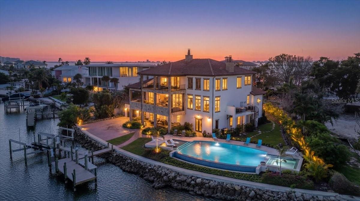 House never flooded, including during Hurricanes Milton and Helene, and protected by a full house generator! 
Lavishly embellished with Old World authenticity, this exceptional waterfront estate evokes the grandeur of a 17th century Tuscan farmhouse. Custom built by John Cannon, the home is set on what was once Ringling’s personal yacht basin, offering protected sailboat water, 180 feet of seawall, a private dock, two boat lifts, and a dedicated kayak lift platform, all framed by sweeping panoramic water views.
From the moment of arrival, the level of craftsmanship is unmistakable. Walls are finished in aged plaster, hand made terra cotta floors have been acid washed and stained to reflect centuries of wear, and authentic frescoes and ceiling beams inspired by the Renaissance period add depth and character throughout. The great room provides a dramatic setting for entertaining with soaring 22 foot ceilings, a gas fireplace, and a wet bar accented by a hammered copper sink.
The chef’s kitchen is equipped with an Italian eight burner gas range and Brazilian soapstone countertops, while the dining room features a rare brick vaulted ceiling that reinforces the home’s Mediterranean soul and creates a truly immersive dining experience. The primary suite is a romantic retreat with his and hers walk in closets and a spa like bath wrapped in rich wood and stone finishes.
Additional spaces include two to three guest bedrooms, dual offices, a bonus room, and a wine room. A true 2,500 square foot ground level garage offers tandem parking for two to four plus vehicles, making it a dream for car collectors.
Outdoor living is exceptional, with stone and wrought iron terraces, an outdoor kitchen and bar on the main level, all designed to capture natural breezes and expansive water views. The newly completed infinity edge pool and spa create a striking visual effect, with the water appearing to seamlessly spill into the bay, while two strategically placed fire pits add warmth and dramatic ambiance after sunset.
This storybook residence is ideally located near Sarasota’s beaches, dining, and cultural attractions, offering a rare blend of architectural artistry, privacy, and timeless elegance.