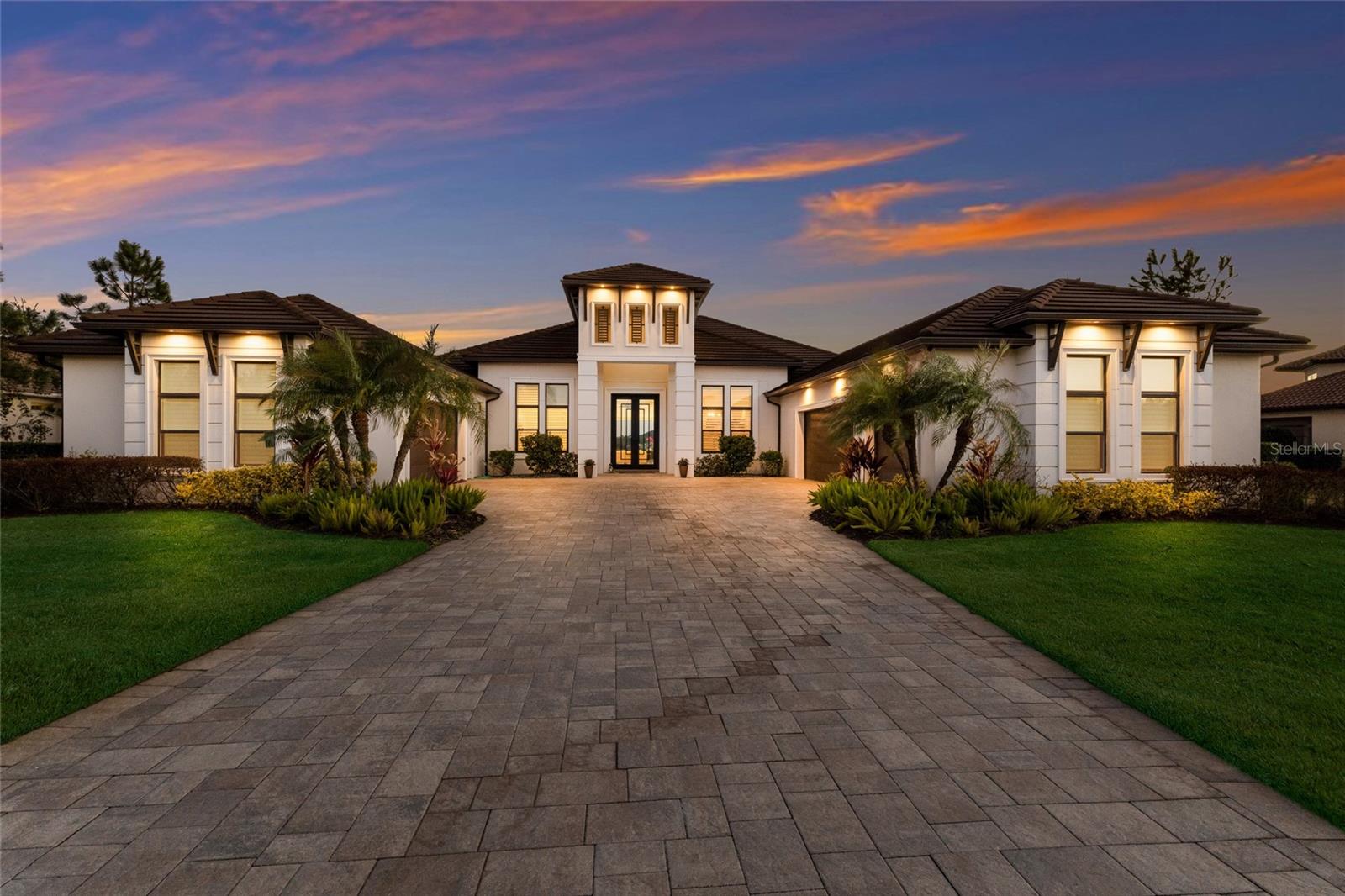 A stately arrival sets the tone for this exceptional custom residence, thoughtfully positioned on over one acre within the gates of The Concession. Blending modern luxury with architectural refinement, the home offers a rare combination of privacy, elegance, and timeless design in one of Lakewood Ranch’s most exclusive communities. Custom double entry doors welcome you into a light-filled interior where engineered hardwood floors anchor the main living spaces and a dramatic wall of sliding glass doors frame serene water views, seamlessly connecting indoor and outdoor living. At the heart of the residence, the chef’s kitchen is both polished and highly functional, appointed with Monogram and Café appliances and anchored by a generous statement quartz island that serves as both focal point and gathering space. Designed to flow effortlessly into the great room and outdoor living areas, the layout supports both elevated entertaining and comfortable everyday living. Architectural elements define the great room, where a custom-designed accent wall showcases intricate detailing, a sleek linear fireplace, and an oversized mounted television, creating a striking focal point that balances warmth with modern design. Tray ceilings throughout further enhance the home’s architectural character, while curated designer lighting, plantation shutters, and a newly installed outdoor surround sound system underscore the thoughtfully executed craftsmanship. The primary suite offers a private retreat of generous proportions, complete with a sitting area and dual custom walk-in closets. The spa-inspired bath features expansive dual vanities, a soaking tub, and a dramatic walk-through shower with triple shower heads, including an overhead rain feature delivering a resort-caliber experience. Two additional guest suites each offer beautifully appointed en-suite baths with elevated design selections tailored for today’s discerning buyer. A private office with oversized windows invites abundant natural light, while the formal dining room is enhanced by a dramatic wine display that serves as a striking focal point for elegant entertaining. A spacious bonus room provides flexible space for recreation, media, or additional guest accommodations. Outdoors, the experience continues with a large pool and spa, expansive covered lanai, and a nicely appointed outdoor kitchen, creating a true resort-style setting. The five-car garage provides exceptional capacity for the automotive enthusiast and additional storage needs, while a fenced yard allows for secure outdoor enjoyment. Constructed with hurricane impact doors and windows throughout and supported by a whole-house generator, the home offers peace of mind with uncompromising quality. This residence masterfully blends functionality with a refined, designer-forward aesthetic, delivering privacy, security, and elevated living. Located just minutes from UTC, Waterside dining and shopping, and the Gulf Coast’s renowned beaches, it offers proximity to everything while maintaining an atmosphere of serene exclusivity. A distinguished offering for those seeking elevated luxury and the true Concession lifestyle.