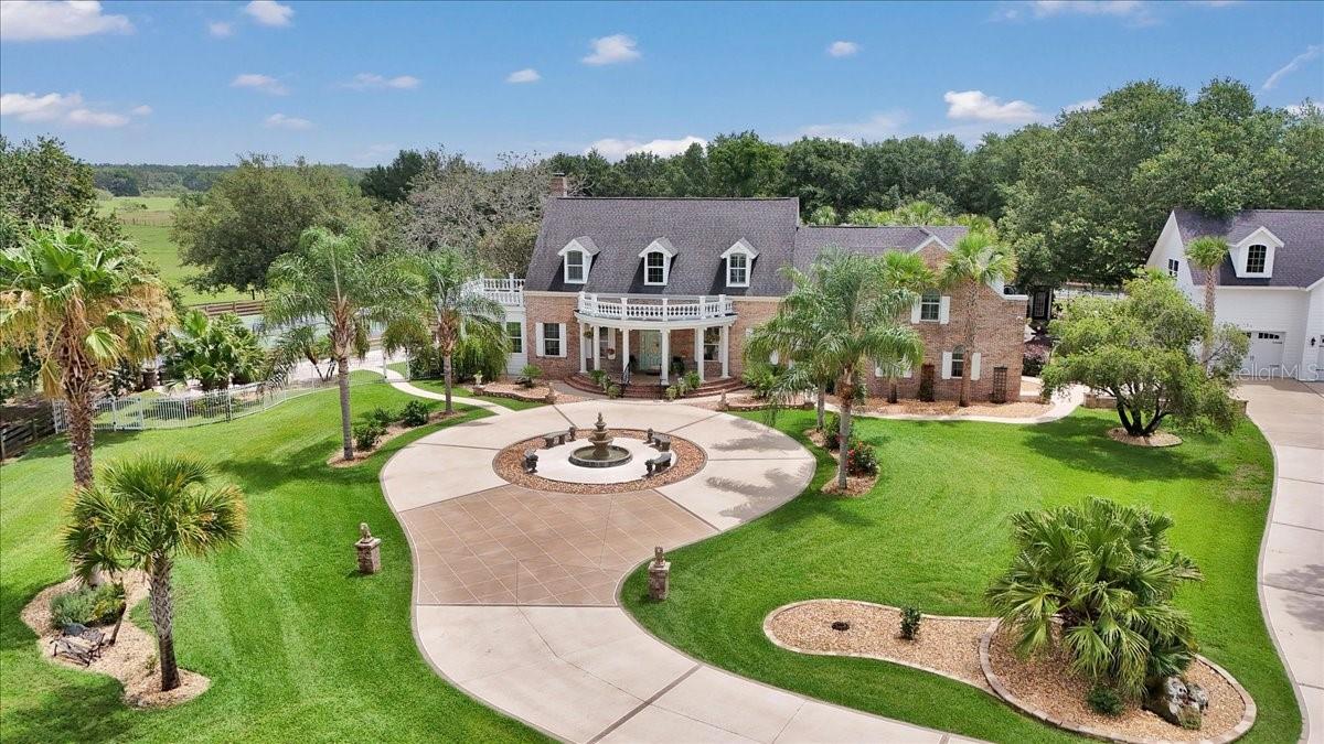 Welcome to paradise in Oxford! This is a rare opportunity to own a one-of-a-kind luxury compound—private, peaceful and ideally within two miles of The Villages. Just five miles from Lake Sumter Landing Market Square, you’ll enjoy easy access to shopping, dining, nightlife, movies and live music. On a beautifully landscaped six-acre corner lot with two gated entrances, this meticulously designed estate offers nearly 9,000 square feet of total living space across multiple structures. The property is the ultimate entertainer’s dream and a private oasis like no other. The main residence features five bedrooms, three full baths and two half baths. The primary suite is on the main floor, along with a formal living room, formal dining room, a cozy family room with gas fireplace, a workout room and all-season sunroom with dual south-facing French doors. The heart of the home is the eat-in kitchen with a Cambria quartz island, ideal for gatherings and everyday living. Upstairs, a bonus family room connects to four bedrooms, one with a private en suite and two sharing a Jack-and-Jill bath. Go outside to your private resort-style retreat featuring an expansive covered lanai, two cabanas, two pickleball courts, an outdoor kitchen, game room, tavern, guest cabin, she shed, man cave, bocce ball and shuffleboard courts. The centerpiece is a concrete/gunite saltwater pool with tile accents, six waterfalls and deck jets—surrounded by lush landscaping, fountains, a peaceful pond, and an oversized pool house with a changing room and fireplace. Car enthusiasts will love the oversized four-car garage with epoxy floors, and upstairs, enjoy a full movie theater and spacious craft room for creative pursuits or additional living quarters. A second detached four-car garage offers even more space for vehicles, ATVs, boats or toys. Several outdoor structures offer flexibility for ADU conversion, making this estate ideal for multi-generational living, potential rental income or luxury guest accommodations. There’s even a beautiful pasture out front so bring a few animals and enjoy the tranquility of country living. Schedule your private showing today and experience this one-of-a-kind compound for yourself.