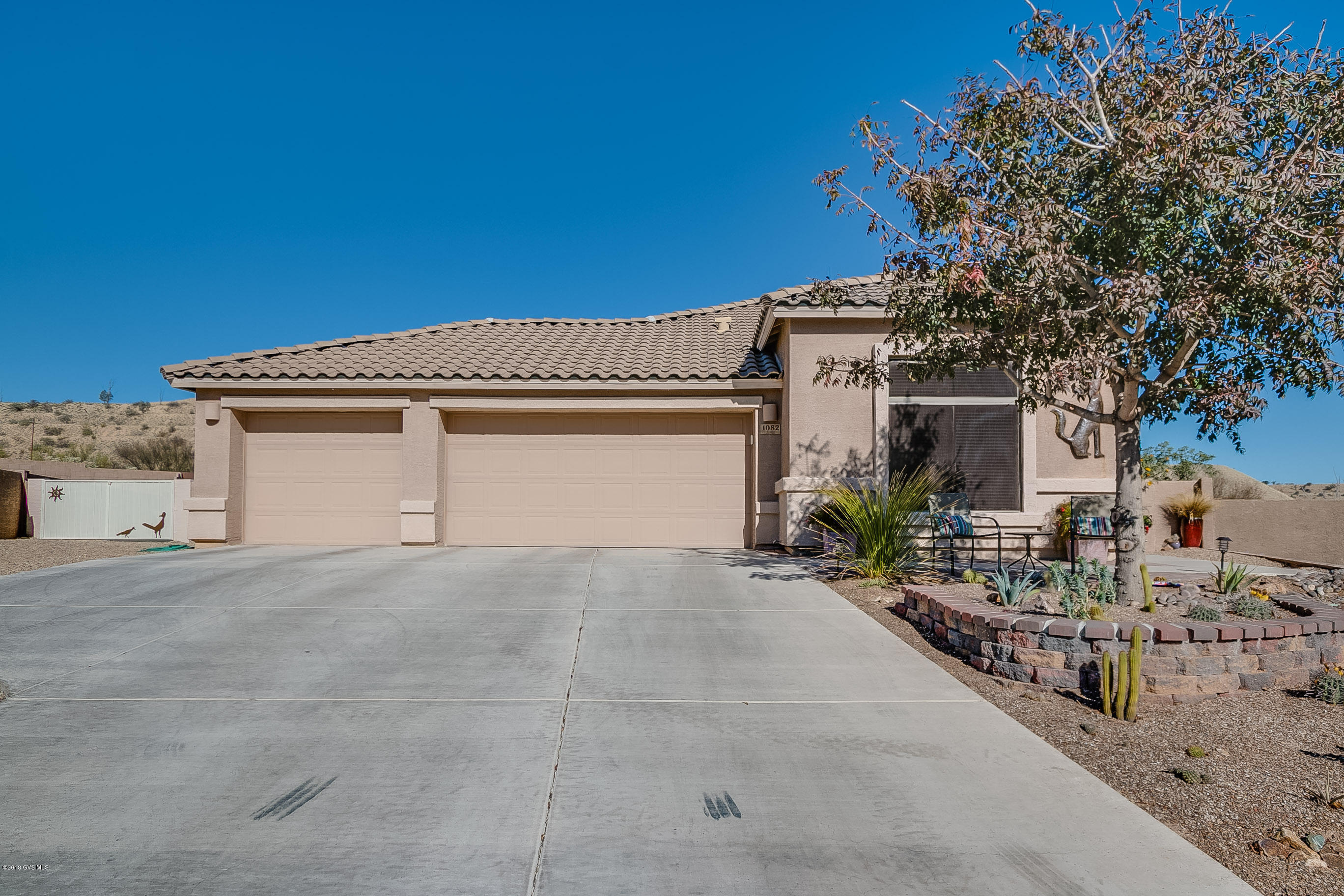 The spaciousness of this home begins with a large 3-Car Garage with double gate providing access to the oversized backyard. The great room wrapped in angles and art niches welcomes you with a sheath of desert tone tile flooring and has cathedral height ceilings for added spatial effect. Pass through the sweeping ceiling archway where your designer kitchen displays beautiful granite countertops accented by a colorful stack tile backsplash complimented by stainless-steel appliances. The prep-cook serving island makes quick snacks easy while the dining area is adjacent making it very convenient for entertaining. Your master bedroom suite gives you enough space for a reading area or exercise equipment. The luxury features continue into the master bath with a granite vanity top, stacked  tile backsplash and an under counter sink for easy cleaning. Contemporary wood-plank tile flooring brings a sense of warmth and peace to your comfy den. Step out to the full length covered patio where a colorful array of paint tones brighten up your outdoor living area and create a wonderful place to relax in the desert air. The vast backyard offers easy care Xeriscape landscaping complete with raised gardens, a brick patio walkway, a cool grassy knoll, a trickling fountain and a custom-built fire pit for fun filled evenings under the star filled skies.