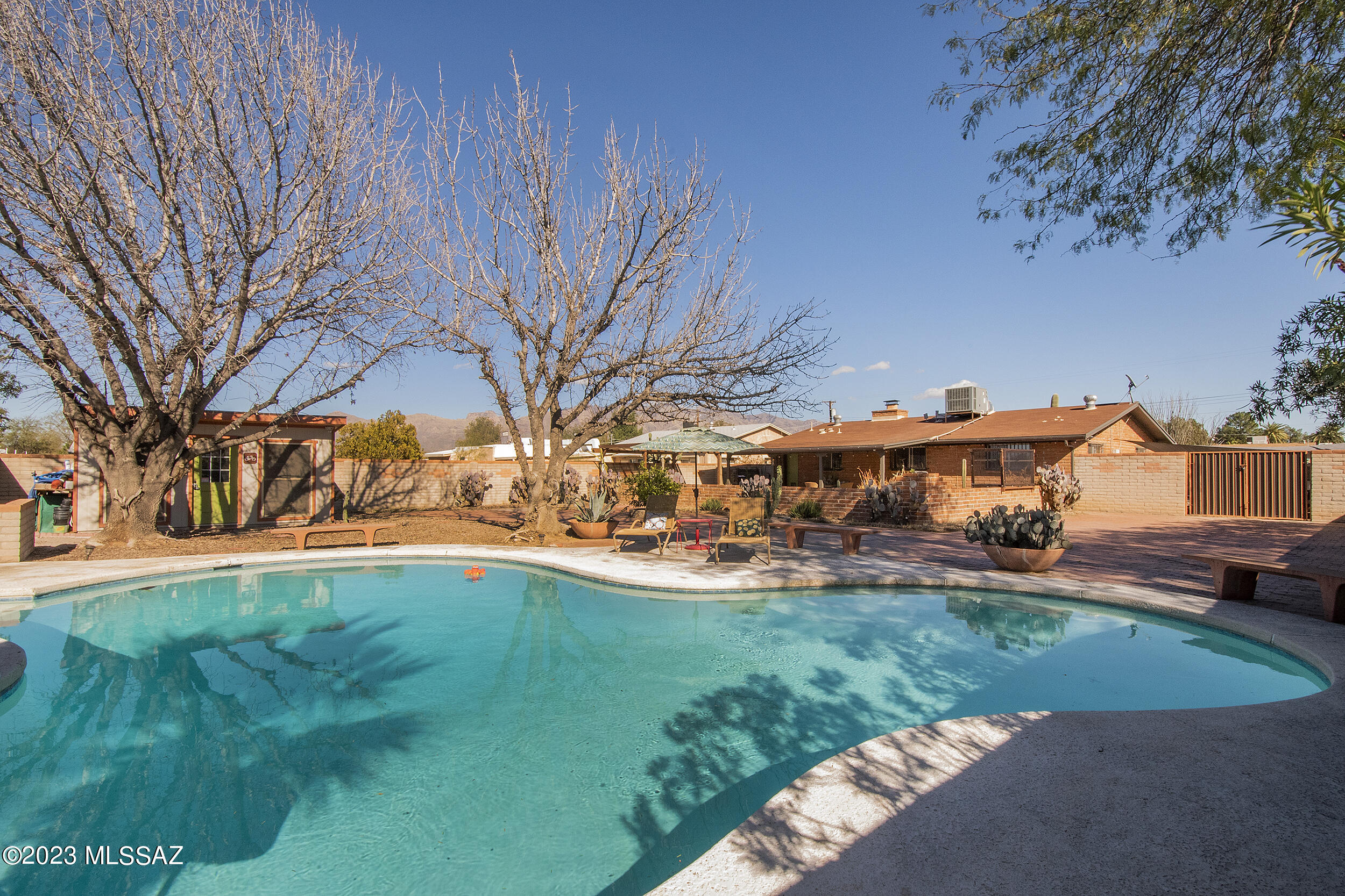 Welcome home to your classic, charming burnt adobe featuring a 3-sided fireplace to enjoy from the kitchen, dining and living rooms. Updates include pebbled walk-in shower in master bath, open kitchen with stainless steel appliances and granite countertops, oversized ceramic tile flooring and dual-paned windows. Step outside to your private oasis with huge sparkling pool, large covered patio perfect for entertaining, separate ramada, custom workshop/storage area, gorgeous mature trees and cacti. Fully enclosed yard with masonry walls also accessible via drive-through metal gate onto extended brick paver area with plenty of room to park an RV. This home is ideally located with proximity to everything: UA, downtown, the Loop, restaurants, foothills, and Amphi schools. Huge quarter-acre R-2 lot for room to expand. Come see for yourself how special this home is!