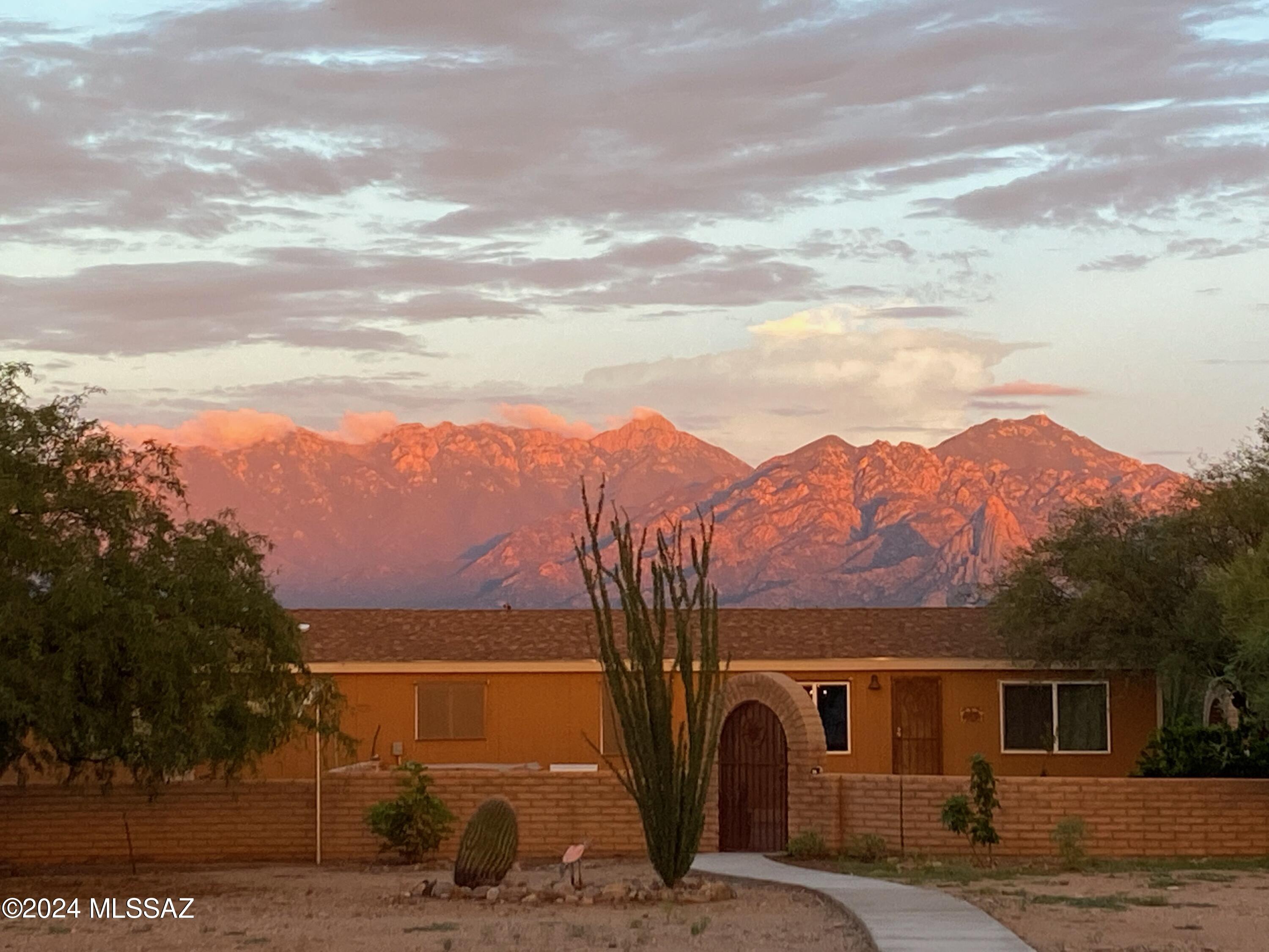 Available now! This lovely affixed mobile home sits on a sprawling 4+ acre lot with fantastic desert & breathtaking mountain vistas! A fenced front yard & a delightful front porch, ideal for enjoying tranquil mornings or afternoon relaxation. Discover a welcoming living room adorned with a decorative ceiling fan, an accented wall, bookshelves, & wood-look tile flooring. The formal family room with outdoor access is perfect for intimate gatherings. The bright eat-in kitchen is equipped w/a farmhouse sink, granite counters, a Travertine tile backsplash, recessed lighting, ample wood cabinetry w/crown molding, a breakfast bar, & a walk-in pantry. Retreat to the main bedroom, offering a private bathroom for convenience. Out the back, you have a hot tub, pavers, fragrant citrus trees, & a detached garage. Massive yard is ready for any horse-friendly activities! Take advantage of this rare find!