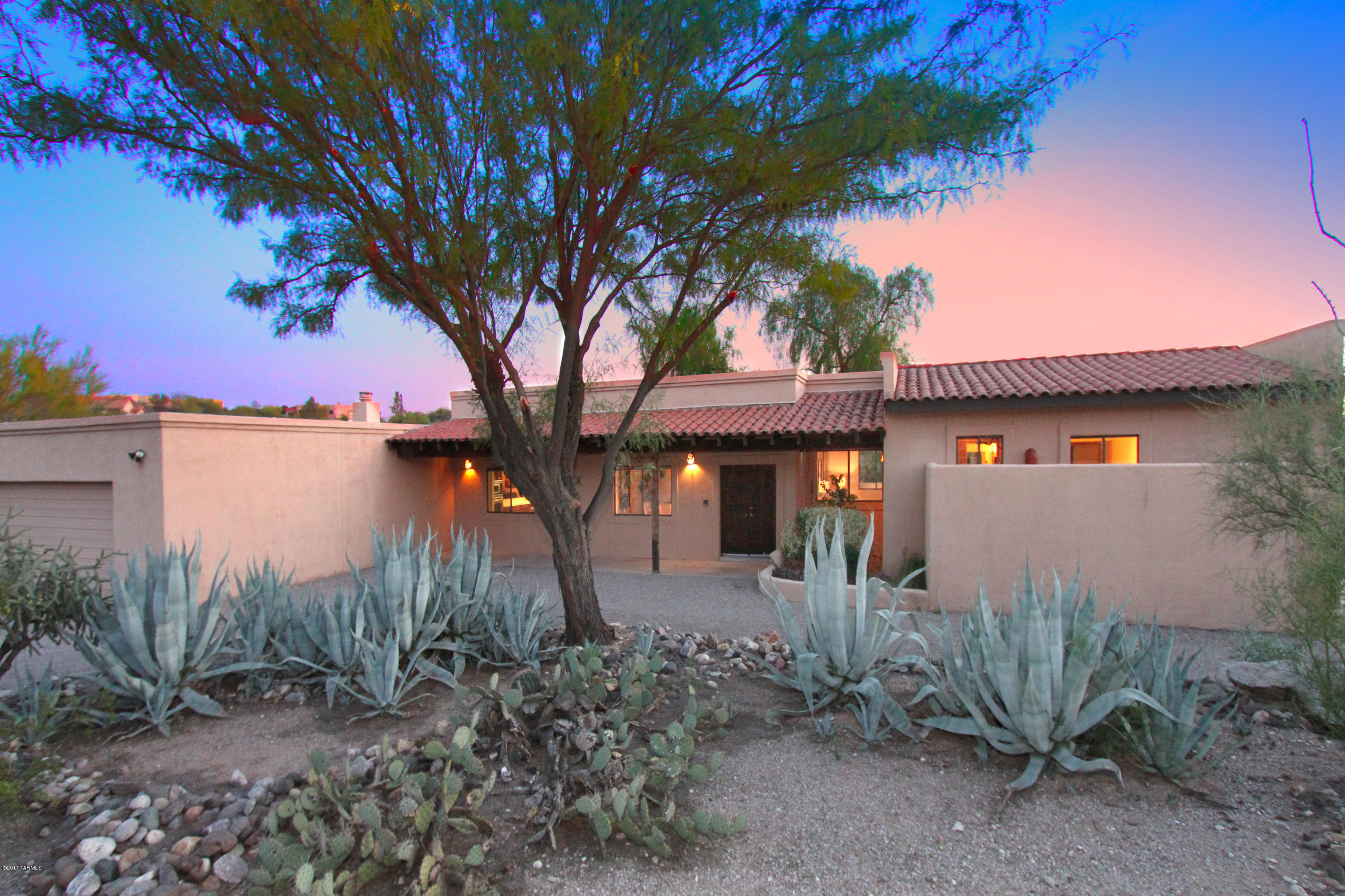 A classic adobe hacienda-style home in the Tucson Foothills awaits its’ new owners. Warm and welcoming, with great spaces for everyone, this home has glorious views both north to the Catalina mountains and south towards sparkling Tucson city lights. A broad front veranda is a perfect place to watch the mountains turn pink as the sun sets. Inside, a comfortable living/sitting room with fireplace has views in both directions, as does the comfortable dining room and spacious kitchen. With classic southwestern tile counters, a large tiled island, breakfast bar and lots of natural light, the kitchen is an easy gathering spot. The adjacent family room with a rustic stone fireplace, long tiled wet bar and wood-beamed ceiling invites the gang to put their feet up and relax. A very generously sized master bedroom with views of downtown opens to an enclosed rear yard graced with fabulous mature weeping willow trees. A large walk-in closet adjoins the bedroom. The master bath is delightful, with sweeping mountain views from the shower and tub, reflected in the mirror that encompassed the span of the long counter with two sinks and a seated make-up area. A wall beyond the bath area provides privacy without blocking the beautiful views. The two additional bedrooms and another full bath are on the other side of the home, creating a very private retreat in the master bedroom. With multiple doors opening from the home, enjoy Tucson's indoor/outdoor lifestyle. A covered rear veranda provides another spot for sunset gazing and relaxed outdoor dinners.  Located on a generous 2/3 of an acre and a corner lot with no neighbors nearby, with District 16 schools and easy access to both downtown Tucson's cultural amenities and the upscale La Encantada shopping and dining mecca, this will be a wonderful home for the lucky buyer.