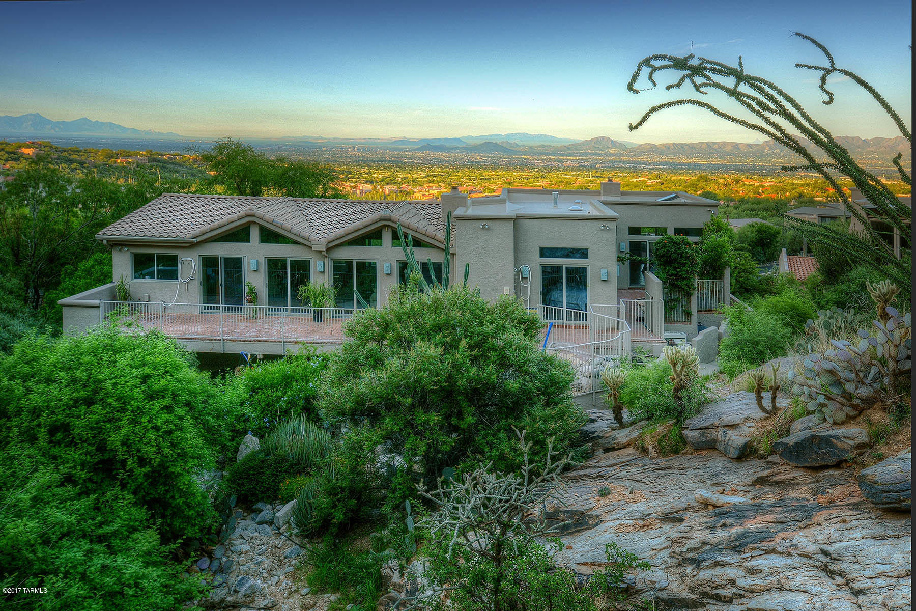 High behind the gates of Sin Vacas you find this home literally nestled in the heart of the Catalinas sitting on 21.56 acres as its backdrop. Make your way to a private driveway lined with mature natural vegetation of high country desert. Upon entering you may visit a private master suite on the first floor, just ideal for visiting guests. Then, depending on your preference, take the brick lined stair well or the elevator to the second floor where you will find a second bedroom and another master bedroom with fireplace and spectacular mountain and city views. On this second floor we find the living room and dining room in a great room setting spanning and hydrologist inspired steel bridge over the canyon wash. Come visit and commune with nature at every turn.