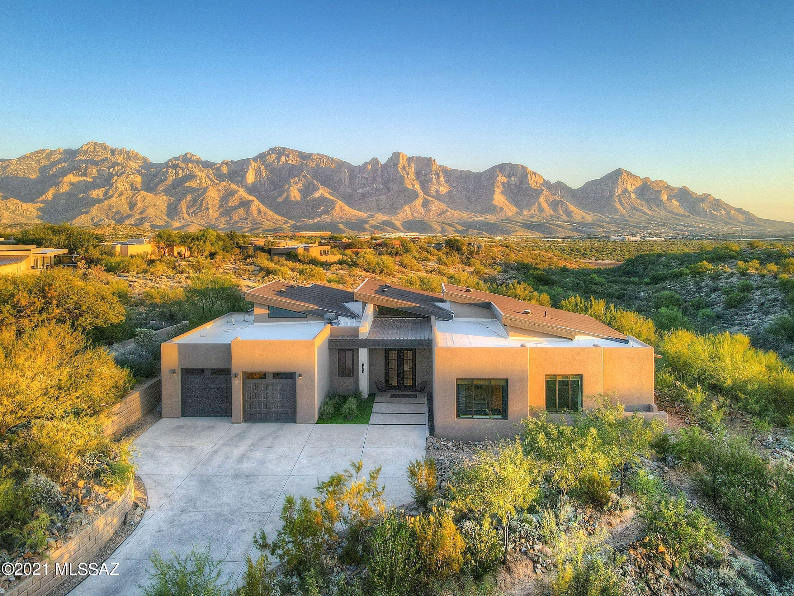 Where else in the world can you own this amazing Contemporary Custom home, nestled in the coveted Oro Valley – High Mesa community? One-of-a-kind astounding Pusch Ridge mountain views are ever present, changing colorful hues from sunrise to sunset from purple, pink, to yellow, each and every day. Upon arrival you are greeted by a private, secure, gated community, with panoramic mountain views as you drive to this beautiful custom 3,291 square-foot custom contemporary home. It embraces 4 bedrooms, 2 bathrooms, chef's kitchen, massive great room with 16 foot ceiling heights, with unobstructed city and mountain views in every direction of the grand Pusch Ridge Mountains through pristine glass walls. This viewing magnificence is carried throughout the property in the kitchen, lush living area and master bedroom. The complete chef's kitchen is a gourmet delight! It's open and easily flowing layout boasts 14 foot ceilings, stainless steel appliances, butler pantry, built-in microwave oven, walnut butcher block and granite countertops. The open kitchen plan naturally flows into the home's great room. Here, you'll find a convenient dining entertainment area, and handy sliding glass doors for a seamless indoor/outdoor living experience overlooking the lap pool. With access to the covered patio, you'll admire custom covered barbecue area with grill which can also be viewed from the sparkling Pebble Tec pool. Inside and out, the breathtaking views of Pusch Ridge are there for the taking, from bright daylight to a stunning display of city lights after dark. The master suite is the epitome of luxurious refuge and repose with custom cornices and room darkening drapes. The master bathroom features porcelain tile, artisan touches, dual sinks, a generous walk-in shower with 2 oversized shower heads and a walk-in closet with customized sectioning. The master suite also offers easy access to the home's patio pool area. This unique contemporary home has something for every family member and guests. As you are viewing this beautiful home, you can see how the roof line is extended around the house to minimize the sun penetrating through the windows and doors.