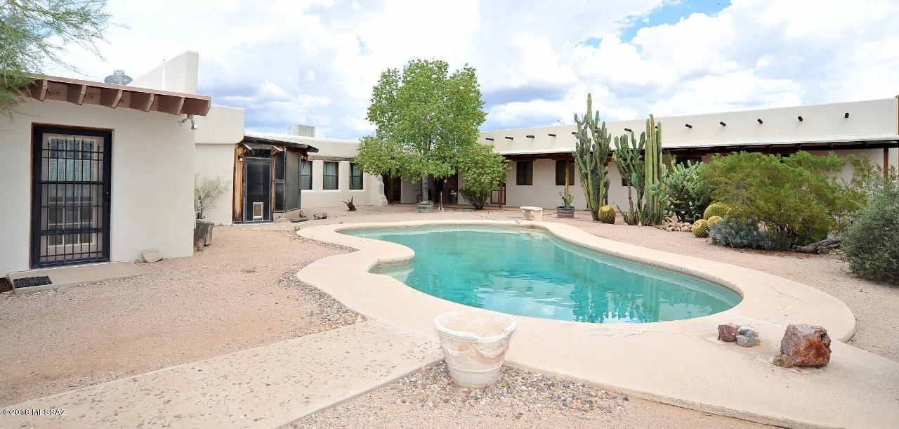 ONE OF A KIND! This unique home has a large open kitchen concept, and a HUGE Adobe family room with exposed wood beams from Mt Lemmon! Plenty of room for a family with a separate master suite, 2 spacious bedrooms with fireplaces, and 3 full baths. Large laundry room features a large walk in pantry. Relax in your beautiful AZ room while watching the kids swim in the pool in the backyard. Or hang out and read a book on the wrap around screened-in porch. Incredible 1,200 sqft workshop with 220amp and 5 sheds on the property allows for plenty of storage space. Workshop also has garage door to store vehicles if needed! 3 car carport off work shop. You can have all of this including 3 acres of fenced, beautiful natural desert.