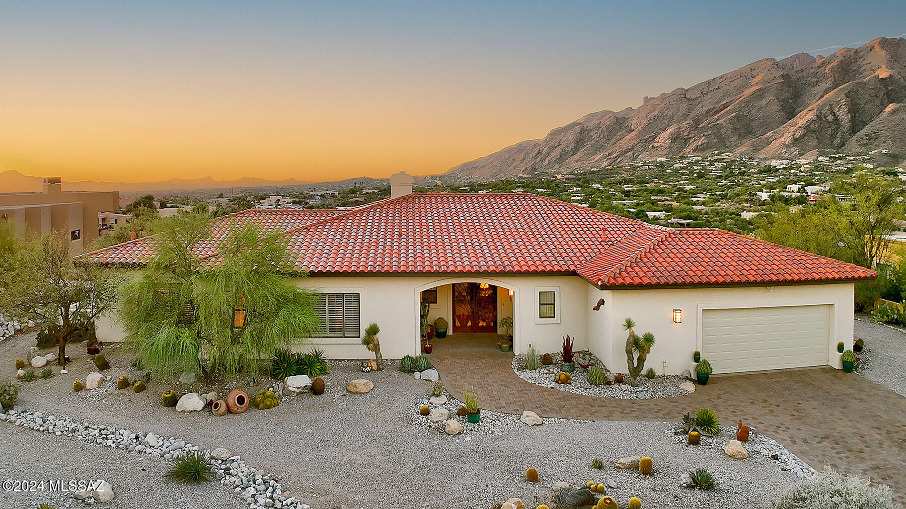 Welcome to this custom-built ranch-style home by LJ McCreary Homes, located in the highly desirable Alta Vista subdivision. Set on nearly an acre, this residence offers stunning panoramic views of the Catalina Mountains and sparkling city lights. A paver driveway with ample guest parking leads to a spacious wrap-around patio, ideal for enjoying the captivating landscape. The welcoming foyer opens to a  large living room where expansive windows and a beautiful fireplace with a custom mantel make a striking impression. A formal dining room provides a perfect setting for entertaining, while the roomy kitchen, featuring granite countertops, dual ovens, pull-out pantry shelves, and abundant oak cabinetry, flows into a cozy eating area. The generous primary suite includes patio access and boasts a spa-like bathroom with a jetted tub, separate walk-in shower, double vanities, and two expansive walk-in closets. Two additional bedrooms - one currently used as an office with engineered wood flooringand a custom desk unit, great for a home office.There are also custom shutters that enhance the natural light throughout the home. Outside, the covered patio immerses you in a serene setting of natural desert plants and unobstructed views. With room to add a pool or custom backyard oasis, this home also features a durable terracotta tile roof, newer water heater, and water softener, ensuring both beauty and longevity. Don't miss this exceptional property!