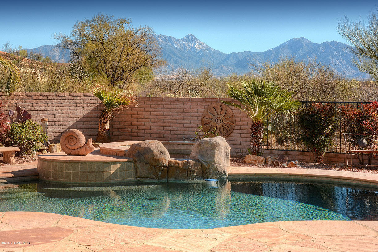 The striking front elevation of this home combines contemporary curved wall and arch top architecture with old world pueblo block accents to let you know that an amazing journey is about to begin. You'll walk through ornate custom copper tone gates to a front courtyard with multi-tone river rock, a trickling fountain and a peaceful sitting alcove. As you enter this exquisite home pause to notice the creative floor plan that blends a great room effect while utilizing a stepped pony wall to offer kitchen and family room delineation. Gorgeous floor tile in unique pattern with multiple shapes streams into an awe inspiring living area with its showcase of lighted art niches, a framed entertainment center, corner fireplace and a dining area with picture window views, all crowned by a  circular recessed ceiling. A serving bar invites your guests into your gourmet kitchen with its dazzling granite slab counter tops and under counter stainless basins, stunning Alder cabinetry incorporating the double door refrigerator, built-in double ovens, large walk-in pantry, a wine cooler and a cooking island with a built-in glass cooktop. Your guests will love the half bath with its custom tile counter top, raised basin and luminary mirror. Flanked by walls of book cases and a built-in murphy bed, your library/den is the perfect place to read your favorite book or keep up with your computer work. Sneak away to your master bedroom sanctuary which features a circular bay window area and a walkout patio door delivering quick access for a refreshing dip in the pool or relaxing in