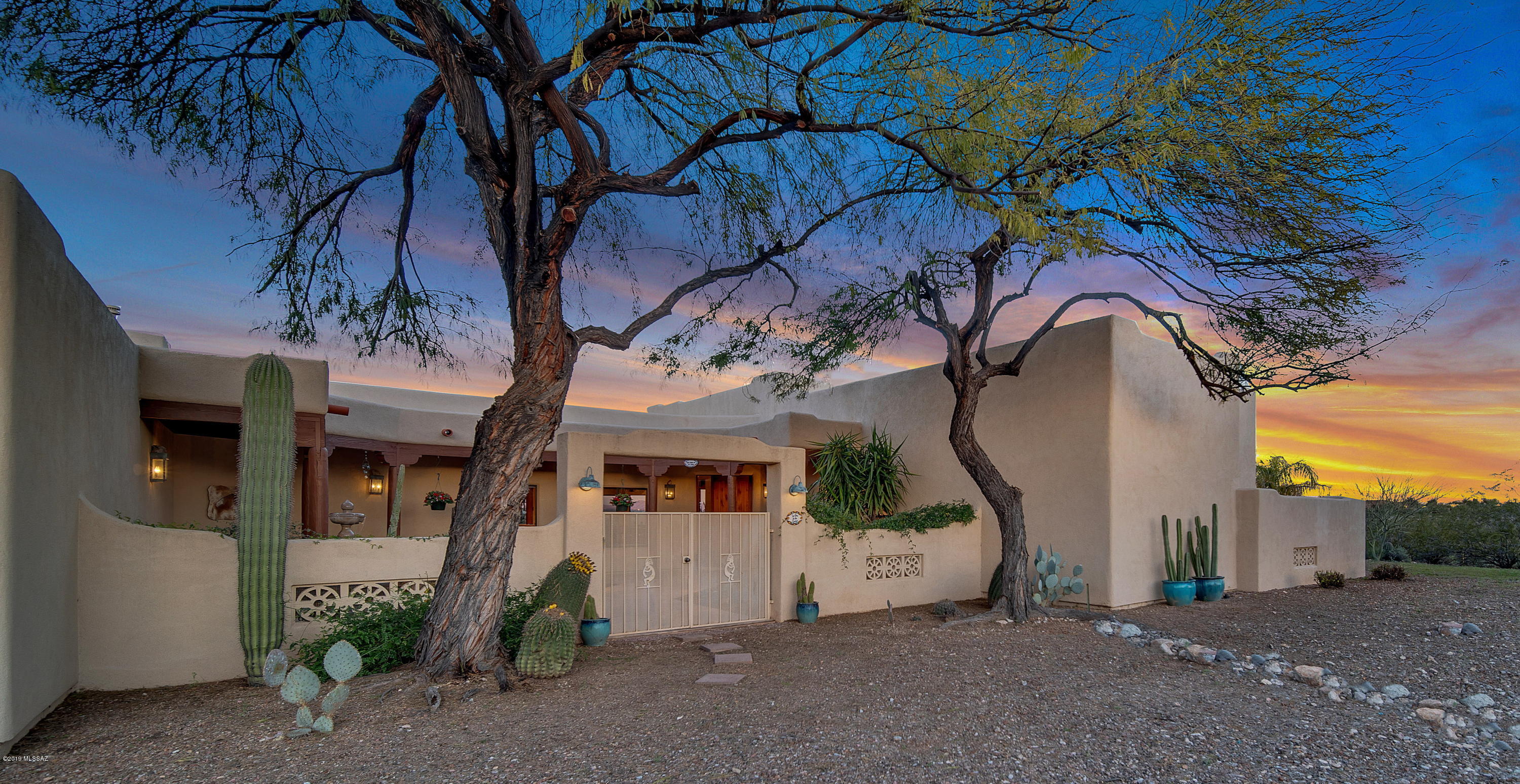 Rural, quiet & private contemporary SantaFe style home w/panoramic views of 4 mountain ranges. Enter through the custom wrought iron gates into the welcoming courtyard w/relaxing fountain & covered patios. The first of many custom details is the front door with its inlaid art and glass-etched panel. The home features custom design elements including Vegas, a plank ceiling in the Great Room, two beehive fireplaces, arches, lighted niches, etched glass accents, and SW-influenced architecture and cabinetry throughout. French doors & large picture windows frame the marvelous views. The kitchen offers a gas burner stove, sink that looks out to the East patio and views beyond, two pantries, wonderful bar-style counter opening up to the dining room & great room. The spacious Master Suite has a jetted tub, roomy separate shower, tons of counter space w/dbl sinks & roomy walk-in closet. The Guest Quarters features a full size bathroom - with a private entrance to the East-facing patio, built-in lighted desk and nice-size closet. Bedrooms 3 and 4 are currently an office & studio. Each offers lighted built-in lighted desk niches. This is a single story home w/no steps. It is zoned as horse property & is convenient to hiking & horse trails. No HOA. The 3-car, 1000sqft garage inc. cabinetry & utility sink. There is a soft water system. The 2000sqft of covered patios wrap around the W, E and S sides of the home offering captivating views of mountains, the valley and the lush desert. The secluded 20' x 60' solar-heated lap pool enjoys equally lovely views. While convenient to I-10, downtown, UofA & Raytheon, this is the ultimate "retreat" - whether relaxing on one of the landscaped patios enjoying the quiet and spectacular views, hiking or horseback riding on the nearby trails, or swimming laps in the solar-heated lap pool - the options are endless ! Please see the Features pages under MLS Documents for more details.