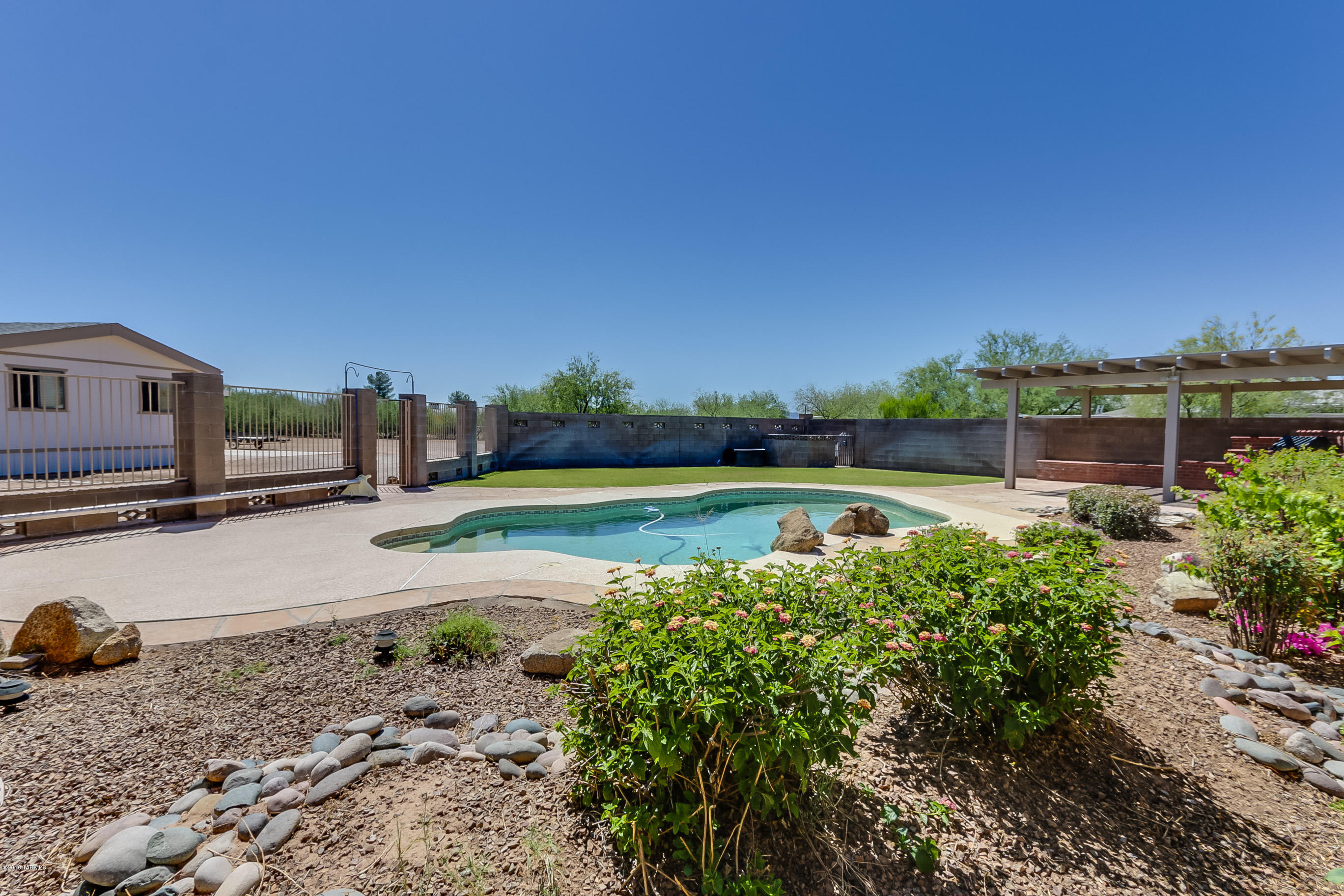 Large private lot with 1440 sq ft, 3 bedroom/2 bath manufactured home, gated pool, covered patio, outdoor kitchen and covered carport.  Well maintained and very clean, this spacious home will not disappoint!  Open and spacious floor plan with large kitchen/BBQ area.  Built-in breakfast bar and desk, fridge included.  Built-in hutch.  Large laundry room with washer and dryer included. Large garden tub in master bath. Newer carpet and wood like floors. Perfect for the hot summers is a gated in-ground pool with grass area and built-in BBQ. Outdoor shed and a 2-car partially covered slab carport