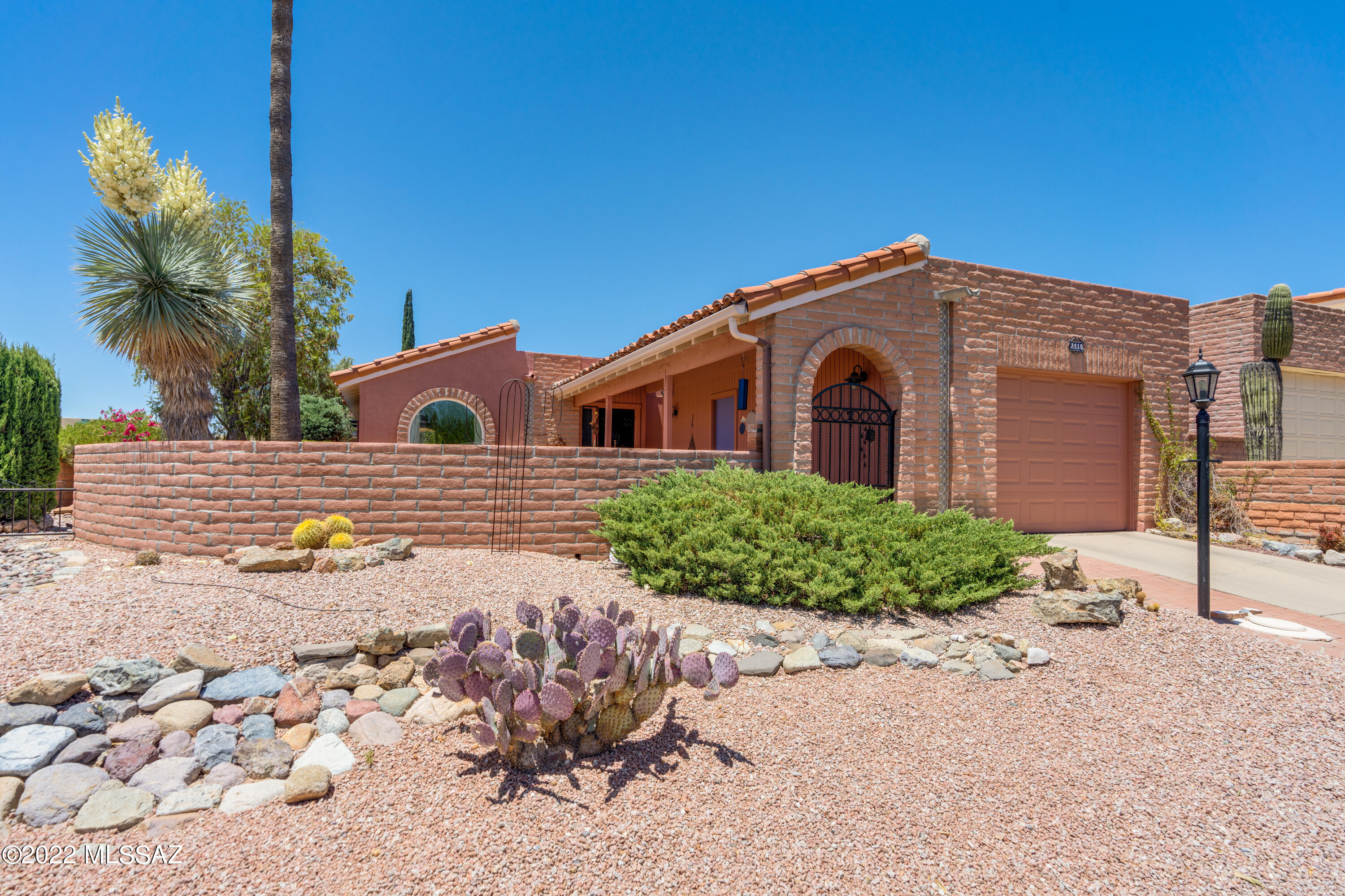 Step past the entry gate to this charming hacienda-style detached home in Desert Hills II, and be enchanted by the expansive front courtyard and gorgeous views of the Santa Rita mountains. This 1,641 sq.ft. 2 BR 2 BA home is bright, updated and upgraded, including a contemporary color palette, newer carpet and luxury plank laminate flooring, and all new vinyl, dual pane windows. Clerestory windows in living room and skylights in all the right places provide plenty of natural light. Kitchen has modern stainless and glass hood over the island cooktop and recessed lighting. Bright Arizona room, Dining Area and Den. Owner's suite has updated bath with newer vanity, lighting and walk-in tile shower. The lush backyard offers plenty of springtime color, shade trees, and a paver patio and ramada.