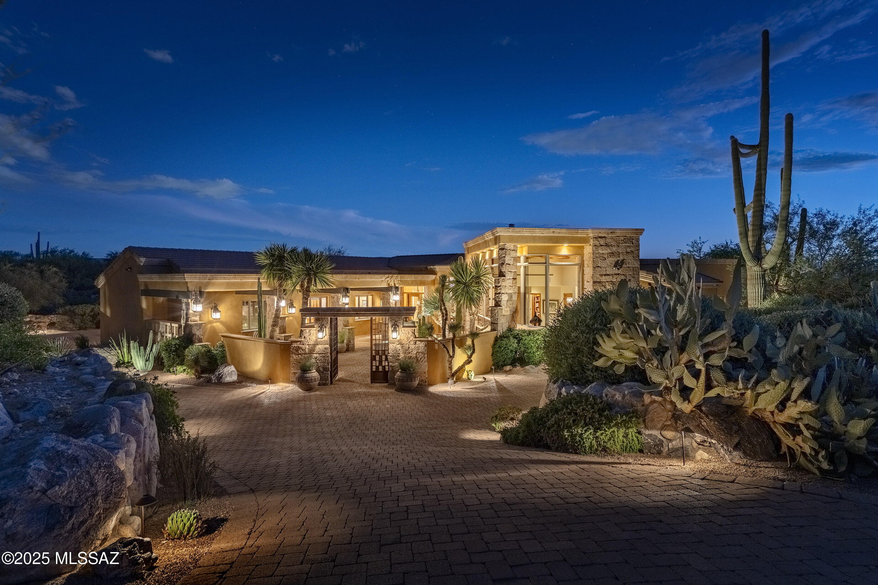 Located behind the private secondary gates of Pima Gardens in Pima Canyon, this architecturally refined desert estate offers privacy, scale, and exceptional design. The property spans 6,631 Sq Ft, including a 5,667 Sq Ft main residence and a 939 Sq Ft detached guest house. A gated courtyard entry with Cantera stone water feature leads to a dramatic foyer with travertine floors, birch-paneled ceilings, and knotty alder beams. The home is thoughtfully laid out to maximize natural light and capture views of the Catalina Mountains and surrounding desert landscape. The formal living room features expansive glass walls, creating a seamless indoor outdoor connection. A climate controlled wine gallery with approximately 900 bottle capacity and an adjacent dining area open directly to outdoor terraces, ideal for entertaining. At the center of the residence, the chef's kitchen features dual islands, imported custom cabinetry, granite countertops, and professional grade appliances, opening to an inviting informal living space with a Cantera stone fireplace. A breakfast nook connects to its own private patio overlooking rock outcroppings, and saguaro-studded terrain. Additional highlights include a dedicated theater designed for an elevated cinematic experience. The primary suite is privately positioned within the west wing and offers a true retreat, featuring custom alder and birch ceiling details, a two way fireplace, a sitting room, and direct access to a private terrace with sweeping desert views. Additional en-suite bedrooms continue the home's consistent level of craftsmanship and finish. The detached guest house provides full independence with its own kitchen, living area, fireplace, and private terrace, ideal for extended guests or multi-generational living.

Outdoor living is exceptional, with expansive Cantera verandas, an outdoor chef's kitchen, multiple courtyards, and 20 foot sliding glass walls that fully retract to create true indoor outdoor flow. The negative edge pool and spa integrate into a one of a kind Cantera water feature with handmade stone spheres and cascading water elements. A lower level turf area adds functional green space for play or gatherings, surrounded by mature desert landscaping and specimen plantings.