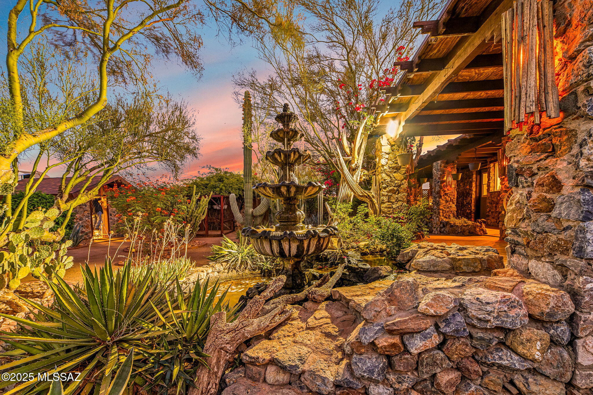 Discover timeless elegance and thoughtful craftsmanship in this custom estate set on spacious acreage, featuring a stunning 100 sq ft guest house and architectural details rarely seen today. With 8-10-inch thick walls adorned in natural stone & cement veneer, the home blends desert beauty with everyday comfort. Step inside to find diagonal-laid flooring, indoor/outdoor living, granite countertops unlike any other, and ambient lighting created from hand-crafted saguaro ribs, setting the tone for desert luxury. The wrap-around deck invites you to relax and take in the serene views of the meticulously landscaped grounds, complete with walking gardens and a grand fountain. Perfect for adventurers & entertainers, the property includes RV hookups, an oversized carport and detached guest space.