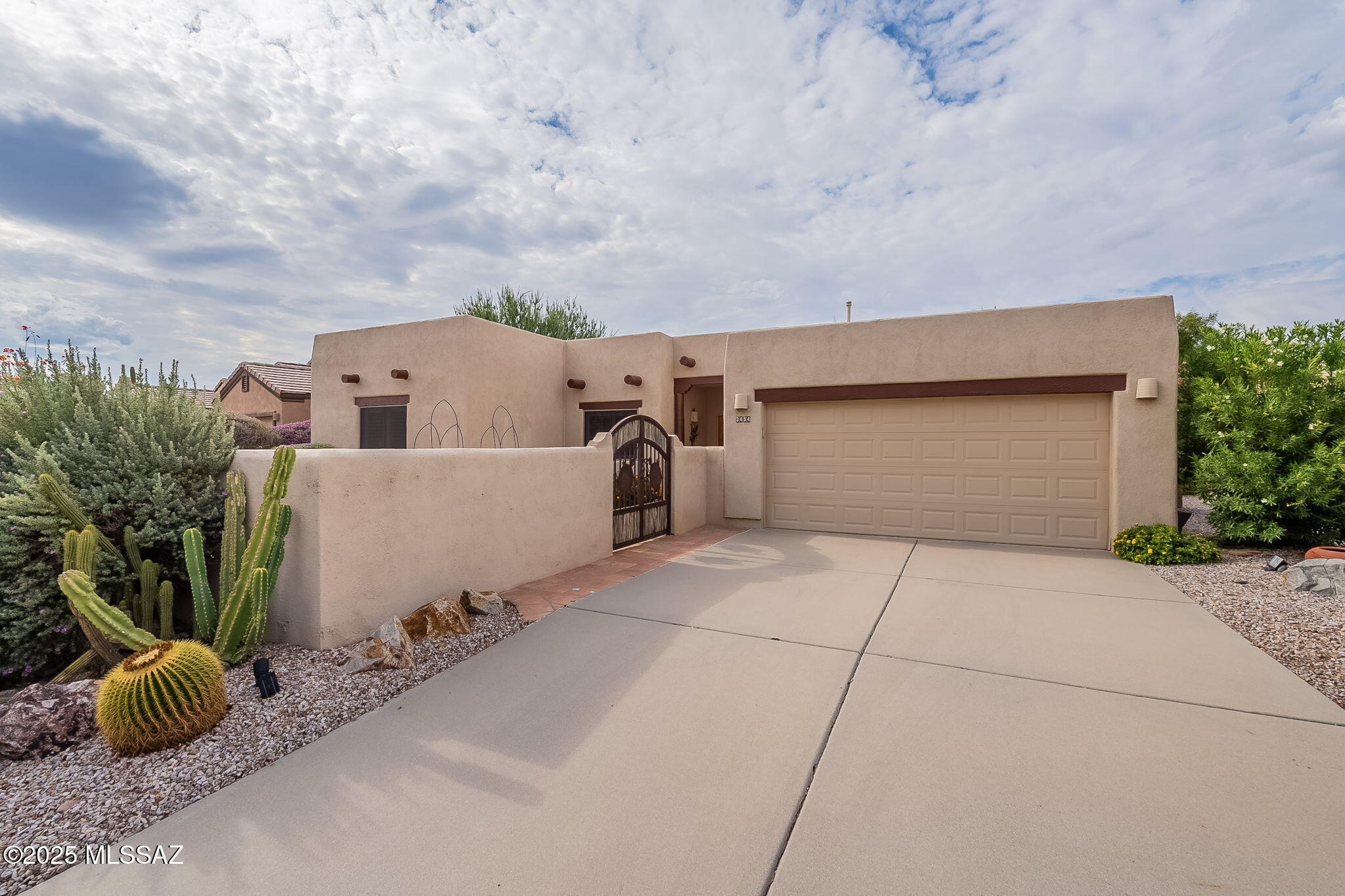 This stunning home is located near the Torres Blancas Golf Club in The Greens gated community and sits directly on the 10th fairway. Beautiful, mature vegetation sets the tone as you arrive, with a long driveway leading to the two-car garage. The front yard is fully enclosed by a walled courtyard with beautiful iron arched gates featuring Sahuaro rib panels for a distinctive southwestern touch. Inside, the courtyard is mostly tiled with areas of decorative rock and desert plants that soften the look, creating the ideal setting for patio furniture where you can sit and visit with friends. The Sante Fe-style home is charming, with a covered front porch and slatted wood entry doors that welcome you inside. Once you enter, you'll notice the tile flooring that runs throughout, giving the home