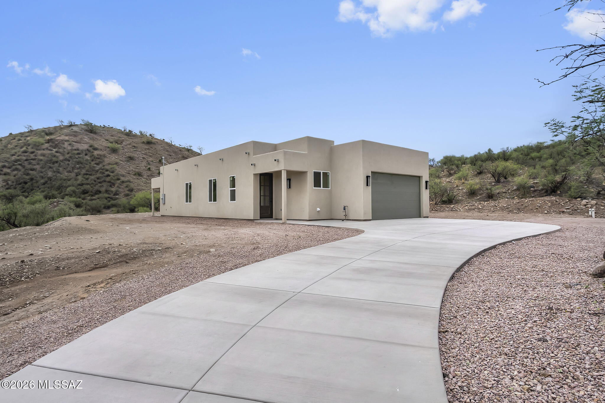 Welcome to 1792 Via San Cayetano in Rio Rico, a stunning new construction home thoughtfully designed with modern finishes, functional living spaces, and exceptional privacy. Situated on a completely flat, fully usable lot, this custom home features an extended curved driveway, durable synthetic stucco exterior, and an impressive 8-foot custom entry door that creates a memorable first impression. Step inside to an open-concept floor plan, filled with abundant natural light. Modern lighting fixtures complement the spacious living areas, high ceilings, while the beautifully designed kitchen serves as the heart of the home. Enjoy a large center island with a convenient pop-up outlet, elegant granite countertops, soft-close cabinetry, sleek black hardware and fixtures, and a generous walk-in pantry that offers both style and functionality. The spacious primary suite provides a private retreat with upgraded 8-foot two-panel doors, luxurious dual vanity with granite countertops, a large walk-in shower, and a custom-designed walk-in closet with thoughtfully spaced shelving to maximize organization and storage. Step outside to the covered back patio and unwind while taking in beautiful mountain views and the peaceful privacy that surrounds the property. Whether you're enjoying your morning coffee or relaxing at sunset, this outdoor space is designed to be enjoyed year-round. Combining quality craftsmanship, modern design, and a highly desirable setting, this custom-built home truly has it all. Don't miss the opportunity to make this exceptional new construction your own.