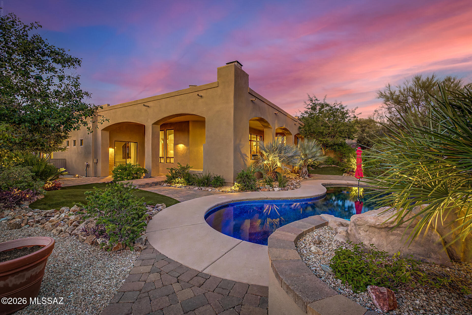 Nestled in the heart of Oro Valley, this private Mediterranean-inspired estate blends refined luxury with effortless resort living. Designed with a desirable split-bedroom layout, the residence offers 4 bedrooms, including 2 ensuite retreats, and 3.5 baths thoughtfully crafted for comfort and privacy. Step through the impressive entry into a stunning Great Room where soaring 12-foot ceilings, a dramatic stacked-stone fireplace, and expansive windows frame sweeping views of the lush backyard oasis. Outdoor living takes center stage with a heated saltwater Pebble Tec pool accented by a cascading waterfall, tropical landscaping, and generous patio spaces designed for year-round enjoyment. Gather around the built-in gas fireplace, host unforgettable evenings at the outdoor BBQ, or dine beneath the stars in a setting that feels like a private resort. The chef's kitchen is equally impressive, appointed with Viking stainless appliances, dual ovens, a gas cooktop, and rich granite surfaces. Adjacent formal dining captures beautiful views of both the desert surroundings and the vibrant backyard retreat, creating an elegant setting for entertaining. Throughout the home, solid 8-foot alder doors and custom alder cabinetry bring warmth, craftsmanship, and timeless character. The secluded primary suite offers a peaceful escape complete with rustic double-door entry, dual vanities, a soaking garden tub, and a beautifully tiled walk-in shower. A second ensuite located near the Great Room provides ideal flexibility for guests, a home office, or private den, while two additional bedrooms are connected by a Jack and Jill bath.  Additional highlights include an oversized 3-car garage, spacious laundry and mudroom with abundant storage, and two separate 50-amp hookups for both RV and spa accommodations. The lagoon-style pool is operated through a Pentair automation system, allowing complete remote control and convenience. Towering palms, flowering vegetation, premium turf, and a dedicated future spa area complete this exceptional desert retreat.