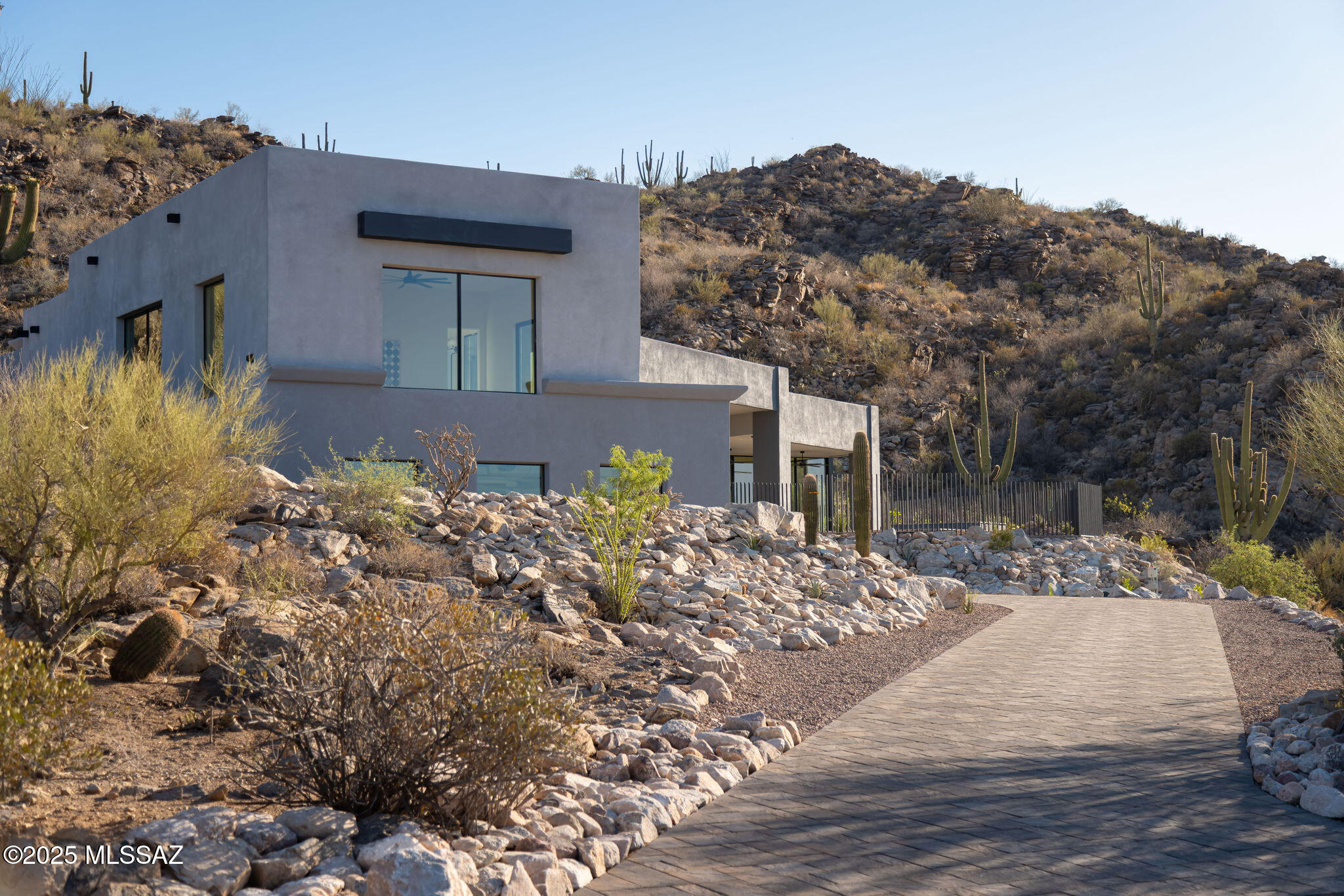 Set against the dramatic backdrop of the Tortolita Mountains, this newly completed residence is located in a private, gated enclave of just thirteen homesites, offering a rare opportunity to live immersed in the desert landscape while enjoying refined modern luxury. Perched above the Tucson Valley with sweeping views of the surrounding mountain ranges, the home was designed for those with a discerning eye for quality, craft, and connection to place.

Constructed in 2025 with energy efficiency at its core, including insulated concrete form (ICF) construction, high-SEER HVAC systems, High performance doors & windows - this residence offers year-round comfort, quiet, and enduring performance. Upon entry, a soaring foyer introduces the home with drama and restraint, setting the tone for what unfolds: a thoughtfully composed interior with a seamless connection to its natural surroundings.

A split-level design allows for a refined balance between scale and intimacy with 16-foot ceilings in the living room, 12-foot ceilings throughout the main level, 10-foot ceilings in the upper level bedrooms and bath. Each space is positioned to capture light, frame views, and flow effortlessly to the outdoors.

The heart of the home is the kitchen, a striking composition of solid surface countertops, custom walnut cabinetry, a steel-clad hood, and a suite of Sub-Zero and Wolf appliances. A walk-in butler's pantry offers generous storage, a wine fridge, and space for further customization. Two distinct living areas add a grounded elegance, spaces designed as much for entertaining as for quiet evenings spent relaxing at home. 

The main suite is a private sanctuary, with sliding doors opening directly to a covered patio with a resort-style pool and an elevated spa. A corner window wraps the bedroom in morning light, and the generously sized bathroom offers natural illumination and intimate views of the desert beyond. 

Four additional en-suite bedrooms are well-placed for privacy and ease of movement throughout. At the upstairs, a private patio off the bedrooms offers a quiet perch to take in the long-range views, city lights by night, mountain silhouettes by day. Built-ins and ample closets are thoughtfully integrated throughout the home, ensuring that storage is as functional as it is discreet.

Outdoor living is an extension of the architecture: the main covered patio includes a built-in outdoor kitchen, perfect for entertaining beside the pool and spa, while shaded porches, dining terraces, and lounging areas are positioned to take full advantage of the sun, shelter, and expansive desert views. All of the outdoor spaces are shaped by the surrounding natural topography and designed to enhance both solitude and connection. 

Ideally located near luxury resorts, restaurants, shopping, hiking trails, and award-winning golf. Minutes from T Bench Bar, two premier golf destinations await. Stone Canyon - a private 1,400 acre community in Oro Valley is ranked among Golf Digest's "Top 100 in America," along with a luxury fitness center, upscale dining, and year-round social events. The Clubs at Dove Mountain combine The Gallery Golf Club and The Golf Club at Dove Mountain, offering two exceptional courses and a single membership in a stunning desert setting. Minutes to I-10 with excellent access to both Tucson and Phoenix airports, this is desert living at its most elevated.