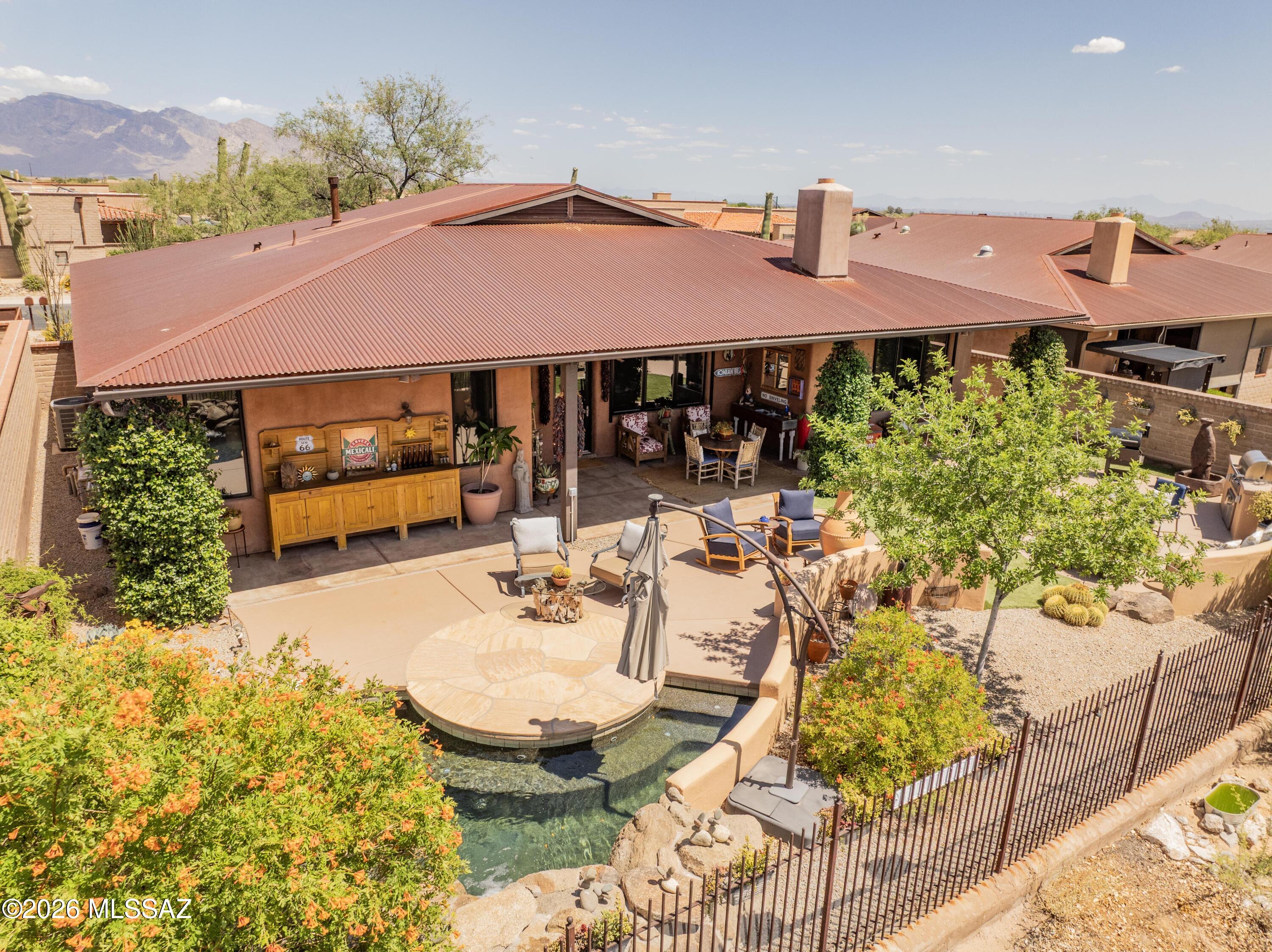 THIS is the home that oozes true Tucson charm. Designed by builder Stellar Gray, this semi-custom ICF with adobe accents sits inside gated Sky Ranch. The front porch greets you with a sitting spot to marvel at the Catalina mountain view. Step inside onto polished concrete floors and 10 1/2 foot tongue and groove pine ceilings. The perfect reading room welcomes you to cozy up for the upcoming monsoons and listen to the rain when it hits the metal roof. The floor plan flows effortlessly into the kitchen where you find quartz   countertops and island, Viking brand gas range, refrigerator and microwave along with a Bosch dishwasher, and stainless farm sink. Dining area is large enough for the gatherings and holidays and the family room with the Rumford fireplace is where stories will be told. Bathrooms have copper sinks and Talavera tile surrounds that will remind you of Old Mexico. Split bedroom layout gives everyone their own peace and quiet. Primary suite sits in the back of the home with a sanctuary feel. Walk in closet, soaking tub, separate shower and double vanity. 
Backyard feels like you are walking out to the "spool" of a local ranch resort. Flagstone, artificial turf and the perfect cooling spot, waterfall included. Built in gas BBQ, covered patio and those famous Tucson sunsets. If you are tired of cookie cutter and want to live your Tucson experience, this is the home for you.