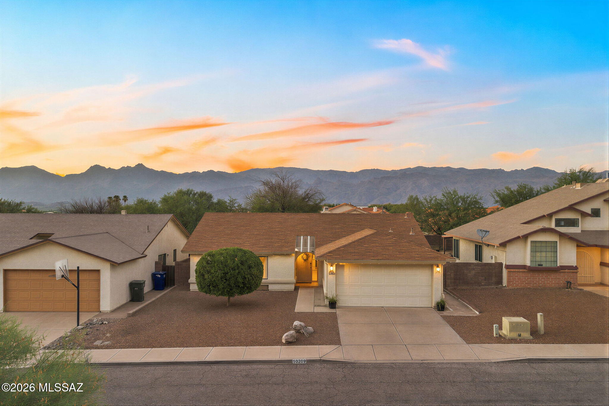 A bright, welcoming home with generous gathering spaces, a fireplace, and a backyard made for Tucson evenings. From the entry, the sunny breakfast nook sits just to the right, while straight ahead the dining area leads into the oversized great room and out through French doors to the deep covered patio. The kitchen pairs warm wood cabinetry with crisp quartz counters, stainless appliances, a gas range, and subway tile. The spacious primary suite includes a dual-sink vanity, while two additional bedrooms offer flexibility for guests, an office, or hobbies. Hard-surface flooring throughout makes upkeep simple. Out back, string lights glow above covered and open-air seating areas, with an expansive paver patio, artificial turf, and a separate dog run completing the easy-care setup. Across the street, a neighborhood desert walking path and sitting area offer a quiet connection to the Sonoran landscape. Additional updates include PEX plumbing throughout and fresh interior paint. With Saguaro National Park East and everyday conveniences within reach, this is a comfortable, thoughtfully updated home that makes everyday living easy.