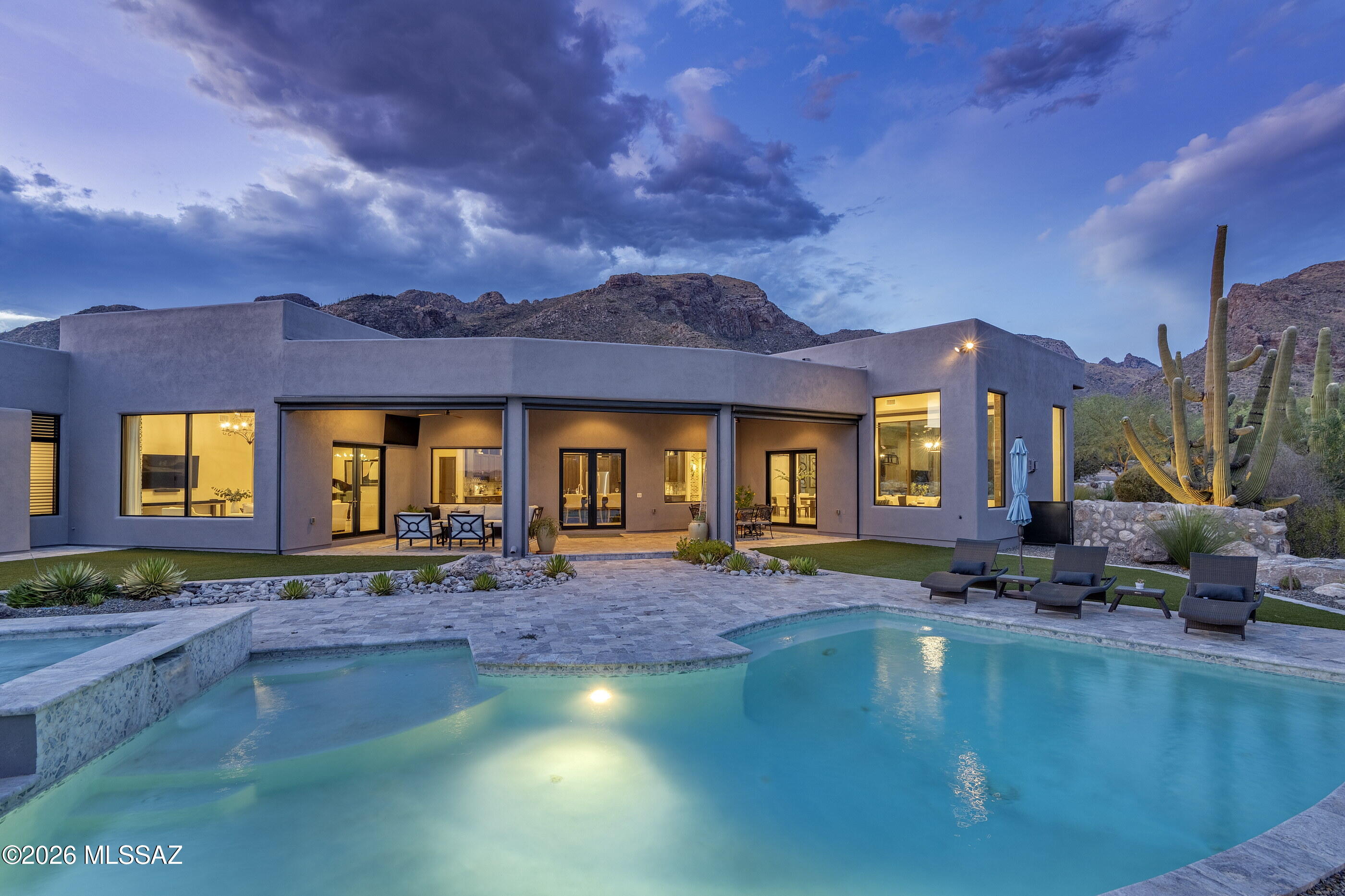 Designed by renowned architect Kevin Howard and completed in 2018, this exceptional contemporary residence is privately situated on a 1.25-acre homesite within the secondary gates of Pima Canyon, one of Tucson's most sought-after guard-gated communities. Framed by sweeping Catalina Mountain views and surrounded by mature saguaros and native desert landscape, the property offers a rare combination of architectural significance, privacy, and modern luxury.

Spanning approximately 5,805 square feet, the single-level floor plan features five ensuite bedrooms, expansive living spaces, soaring 16-foot ceilings, and walls of glass that capture the surrounding mountain vistas while filling the home with natural light. A dramatic Victory Metal Works iron and glass entry door establishes an immediate connection to the desert setting and introduces the home's sophisticated contemporary design.

The formal living and dining rooms were designed for both everyday living and refined entertaining, anchored by a striking floor-to-ceiling porcelain tile fireplace. Large-format porcelain flooring, exposed wood beams, motorized window coverings, and 8-foot alder doors throughout reflect the home's exceptional level of craftsmanship and attention to detail.

At the heart of the residence, the chef's kitchen combines functionality with designer finishes. Custom cabinetry offers extensive storage and organization, complemented by Calcutta and Fossil Gray quartz countertops, a Marrakesh porcelain tile backsplash, a fireclay apron-front sink, oversized center island, and a spacious walk-in pantry. Premium Bertazzoni Professional Series appliances include a 48-inch six-burner gas range and dual 36-inch French door refrigerator/freezer, creating an ideal environment for both casual meals and large-scale entertaining.

The primary suite serves as a private retreat, distinguished by rich hickory plank flooring, exposed wood beam ceilings, a secluded patio overlooking the desert landscape and Catalina Mountains, and a spa-inspired bath finished with floor-to-ceiling marble surfaces. Additional features include a freestanding soaking tub, walk-in shower with multiple shower heads, dual vanities with Cashmere Carrera quartz countertops, a dedicated makeup vanity, and a spacious walk-in closet with integrated washer and dryer. Four additional ensuite guest bedrooms provide exceptional accommodations for family and visitors.

Outdoor living is equally impressive. The resort-style backyard was thoughtfully designed to embrace Tucson's year-round climate, featuring expansive patios, multiple lounging areas, a sparkling pool and spa with spillway, professionally designed desert landscaping, natural boulder accents, artificial turf, and unobstructed Catalina Mountain views. Remote controlled sun screens enhance comfort throughout the outdoor living areas, creating inviting spaces for both relaxation and entertaining.

A consistent commitment to care and maintenance is evident throughout the residence. Three Trane HVAC systems service the home, providing efficient, zoned climate control, complemented by an owned solar photovoltaic system that enhances long-term energy efficiency. Additional highlights include a 1,493-square-foot four-car garage with extensive built-in cabinetry, a brick cobblestone driveway, and exterior enhancements such as repainting and a full roof re-coating completed in September 2025.

Combining award-winning architecture, contemporary design, premium construction, and breathtaking Catalina Mountain views, this remarkable Pima Canyon residence represents a rare opportunity within one of Southern Arizona's premier luxury communities.