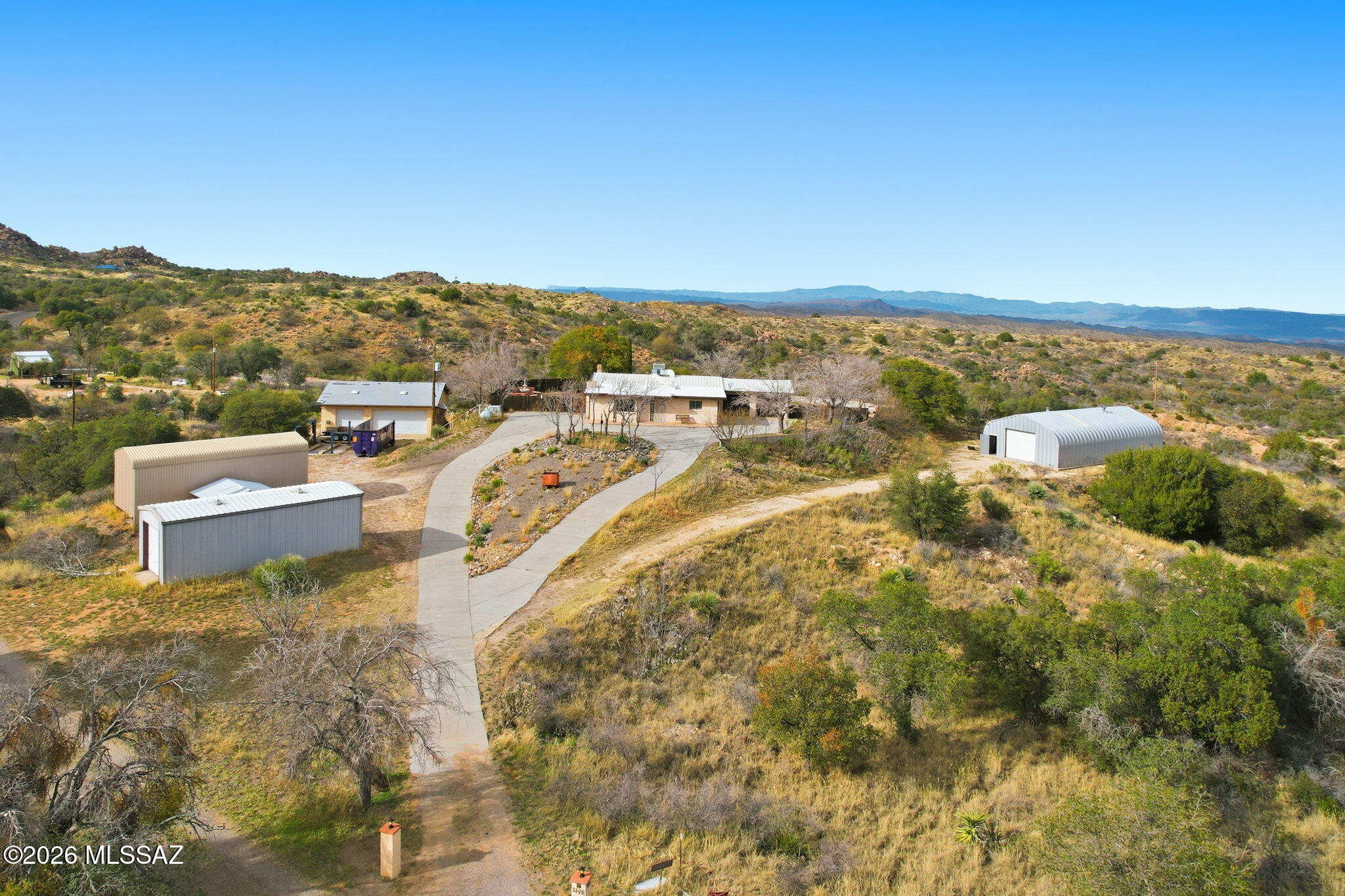 Set on 8.5 sweeping acres in the quiet Holycross Canyon area, this Oracle retreat blends rustic charm with rare, hard to find garage and workshop capacity perfect for collectors, hobbyists, or anyone craving space, privacy, and panoramic mountain views. The single level 1,730 sq ft home welcomes you with a warm, inviting living room anchored by a wood-burning fireplace  and framed by beamed ceilings and natural light. The kitchen offers an island, electric cooktop and oven, pantry closet, and easy flow into the dining area and custom wet bar, complete with running water and a small refrigerator ideal for entertaining without interrupting the cook.

An enclosed Arizona room extends your living space and creates a peaceful spot to take in the sunrise, sunset, and endless mountain vis vistas that define this property. Two bedrooms plus den and two baths include a primary suite with a shower only layout and an additional bath with shower/tub combo. 
Outdoors, the property truly shines. A fenced serenity garden offers a safe space for pets or little ones, while the surrounding natural desert landscape enhances the sense of privacy. Car enthusiasts and makers will appreciate the detached workshop with electric, attached cabinetry, and extended 3 garage/workshop, plus an electric car lift outside and multiple RV options: a detached RV carport, an enclosed RV garage with manual doors on both sides, and a detached 9 car garage (no electric) for unmatched storage and flexibility. Additional features include a private well, propane, septic, paved concrete driveway, and a whole house gas powered generator for peace of mind.
Whether you're seeking a private desert homestead, a workshop ready property, or a peaceful getaway with room to roam, this one of a kind Oracle gem offers space, views, and versatility rarely found at this price point.