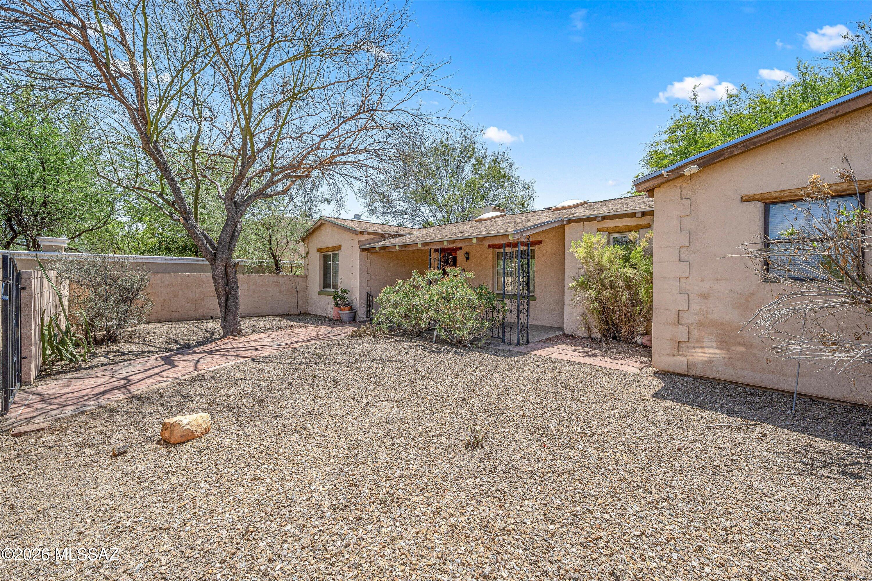 Built in 1941, this 4-bedroom, 2-bath home reflects the character and charm that define Tucson's historic neighborhoods. Nestled beneath mature shade trees on a 0.34-acre lot in the heart of Central Tucson, the property offers a pool, no HOA, and a location that's hard to beat. A circular driveway, gated courtyard, and welcoming front porch create a memorable first impression, while the spacious lot provides room to relax, entertain, and enjoy Tucson's outdoor lifestyle. 
At the center of the home, the kitchen combines functionality and character with abundant cabinetry, granite countertops, pendant and recessed lighting, black appliances, and an electric range. The adjoining dining area creates an easy flow for meals, gatherings, and everyday living.
The spacious living room showcases a a wood-burning fireplace, custom built-in shelving, skylights, and abundant natural light. The thoughtfully designed floor plan offers comfortable gathering spaces while maintaining privacy between the primary suite and secondary bedrooms. 
The private primary suite features a large walk-in closet and an updated ensuite bath with a beautifully tiled walk-in shower. Three additional bedrooms provide flexibility for guests, hobbies, workspace, or other needs. A separate laundry room adds everyday convenience. 
Step outside to enjoy the oversized backyard, complete with a pool, covered patio, mature landscaping, and plenty of room to relax, entertain, garden, or simply enjoy Tucson's beautiful weather. A detached garage and storage shed provide additional storage and workspace options, while the 0.34-acre lot offers room to spread out in the heart of Central Tucson. 
Located in the desirable Broadway Village area, you'll enjoy convenient access to the historic Broadway Village Shopping Center, locally owned restaurants, coffee shops, parks, the University of Arizona, Banner University Medical Center, and downtown Tucson. Rooted in Tucson's rich history, the area is known for its distinctive architecture, mature trees, and central location, offering a blend of character and convenience that is uniquely Tucson.