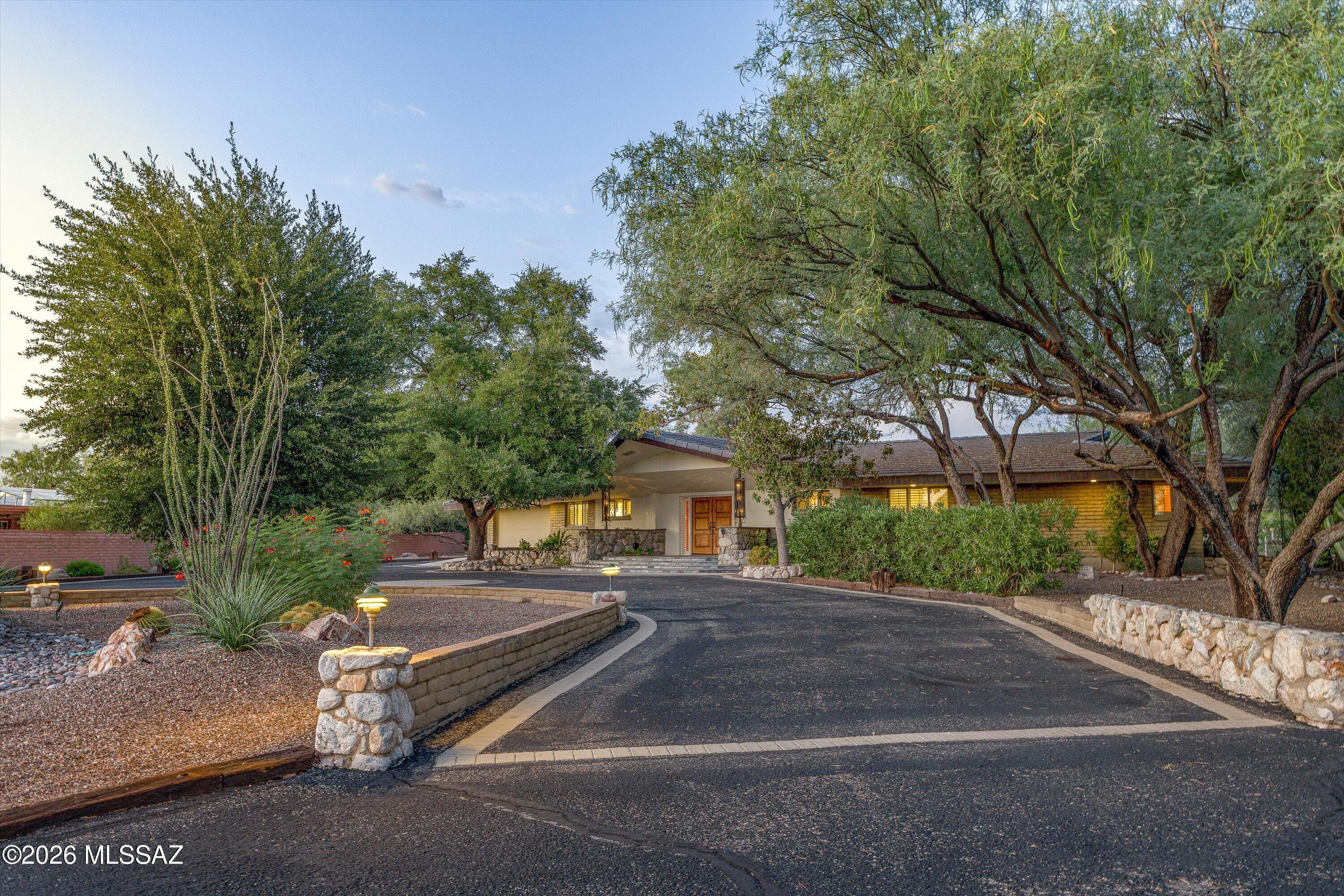 Nestled on .83 acres in the prestigious Oro Valley Country Club, this one-owner custom three-bedroom, three-bath residence offers an exceptional blend of timeless Southwestern architecture, privacy, and breathtaking golf course living. Ideally positioned along the 1st fairway, the home captures sweeping golf course views, magnificent Catalina Mountain vistas, and spectacular Arizona sunrises from its premier homesite.
A graceful circular driveway winds beneath towering, mature trees to a dramatic covered entry with custom wood double doors and stone accents, welcoming you into this beautifully maintained 2,693-square-foot home. Designed for both everyday living and effortless entertaining, the spacious great room features soaring vaulted ceilings, abundant natural light, a dramatic floor-to-ceiling river rock fireplace, and custom built-in cabinetry that provides both elegant display space and additional storage. Plantation shutters and French doors create a seamless connection to the expansive covered patio while showcasing picturesque golf course views.

The updated galley-style kitchen combines warmth and functionality with rich custom wood cabinetry, granite countertops, stainless steel appliances, generous workspace, and a convenient planning desk. A large picture window above the sink overlooks the patio, fairway, and Catalina Mountains, while direct patio access. 
The spacious primary suite is a private retreat with room for a sitting area, French doors opening to the patio, plantation shutters, crown molding, and a luxurious ensuite bath featuring dual vanities, extensive custom cabinetry, stone countertops, and a spacious walk-in shower with multiple shower heads.

Designed to capture Arizona's spectacular lifestyle, the patio features a custom stone fireplace, built-in stainless-steel barbecue, elevated spa, and multiple seating areas overlooking the lush fairway.  Whether enjoying a quiet morning coffee as the sun rises over the Catalina Mountains or entertaining beneath Arizona's colorful skies, this remarkable backyard delivers year-round resort-style living.

The property also includes an attached two-car garage plus extensive additional parking, offering ample space for multiple vehicles, guests, or recreational vehicles.

Enjoy country club living, whether it's a round of golf, pickleball, a relaxing walk around the community, a bike ride on the popular 131-mile multi-use "Loop," or the convenience of dining and shopping.  Make this home yours today
