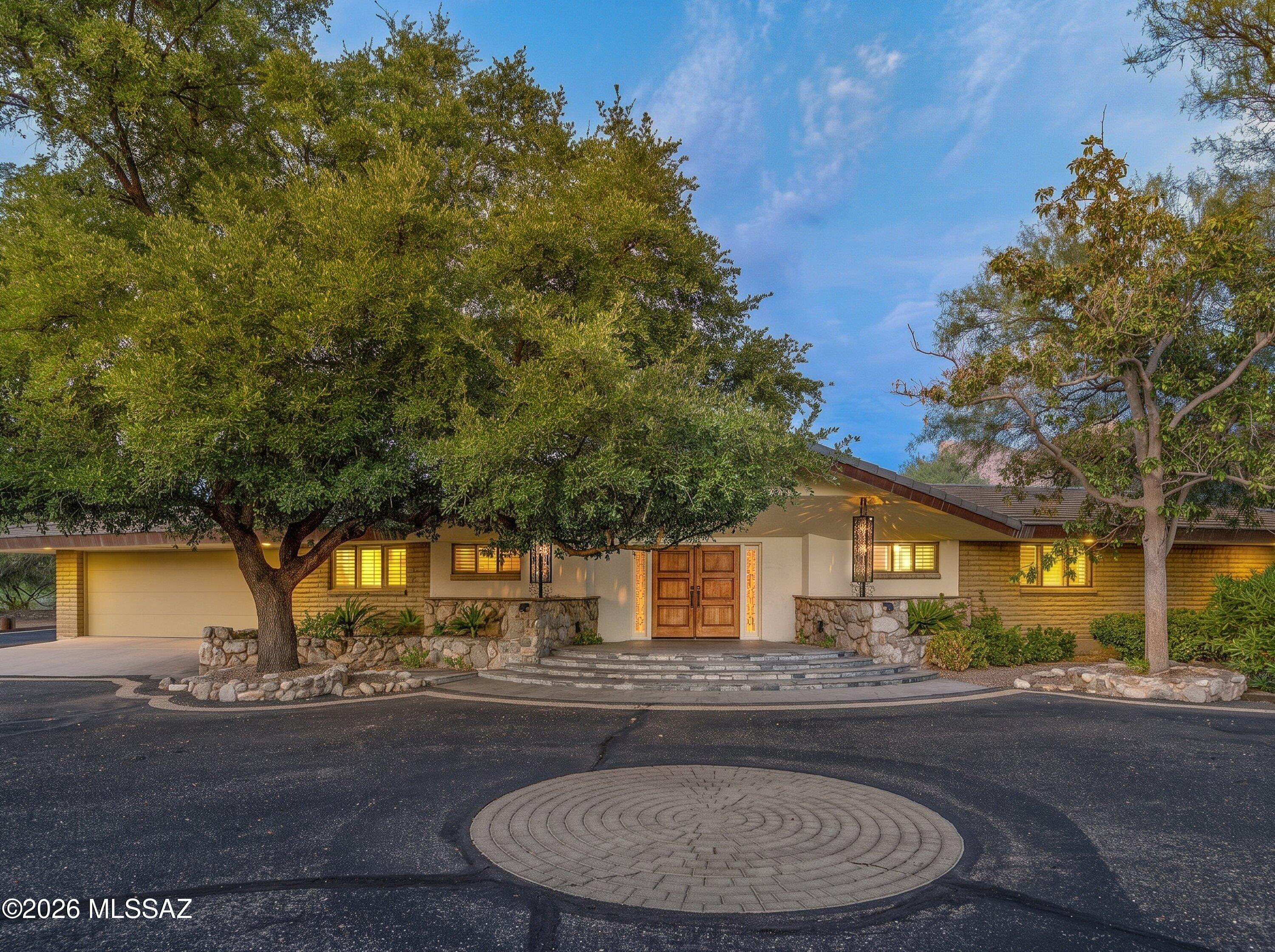 Nestled on .83 acres in the prestigious Oro Valley Country Club, this one-owner custom three-bedroom, three-bath residence offers an exceptional blend of timeless Southwestern architecture, privacy, and breathtaking golf course living. Ideally positioned along the 1st fairway, the home captures sweeping golf course views, magnificent Catalina Mountain vistas, and spectacular Arizona sunrises from its premier homesite.
A graceful circular driveway winds beneath towering, mature trees to a dramatic covered entry with custom wood double doors and stone accents, welcoming you into this beautifully maintained 2,693-square-foot home. Designed for both everyday living and effortless entertaining, the spacious great room features soaring vaulted ceilings, abundant natural light, a dramatic floor-to-ceiling river rock fireplace, and custom built-in cabinetry that provides both elegant display space and additional storage. Plantation shutters and French doors create a seamless connection to the expansive covered patio while showcasing picturesque golf course views.

The updated galley-style kitchen combines warmth and functionality with rich custom wood cabinetry, granite countertops, stainless steel appliances, generous workspace, and a convenient planning desk. A large picture window above the sink overlooks the patio, fairway, and Catalina Mountains, while direct patio access. 

The spacious primary suite is a private retreat with room for a sitting area, French doors opening to the patio, plantation shutters, crown molding, and a luxurious ensuite bath featuring dual vanities, extensive custom cabinetry, stone countertops, and a spacious walk-in shower with multiple shower heads.

Designed to capture Arizona's spectacular lifestyle, the patio features a custom stone fireplace, built-in barbecue, elevated spa, and multiple seating areas overlooking the lush fairway.  Whether enjoying a quiet morning coffee as the sun rises over the Catalina Mountains or entertaining beneath Arizona's colorful skies, this remarkable backyard delivers year-round resort-style living.

The property also includes an attached two-car garage plus extensive additional parking, offering ample space for multiple vehicles, guests, or recreational vehicles.

Enjoy country club living, whether it's a round of golf, pickleball, a relaxing walk around the community, a bike ride on the popular 131-mile multi-use "Loop," or the convenience of dining and shopping.  Make this home yours today