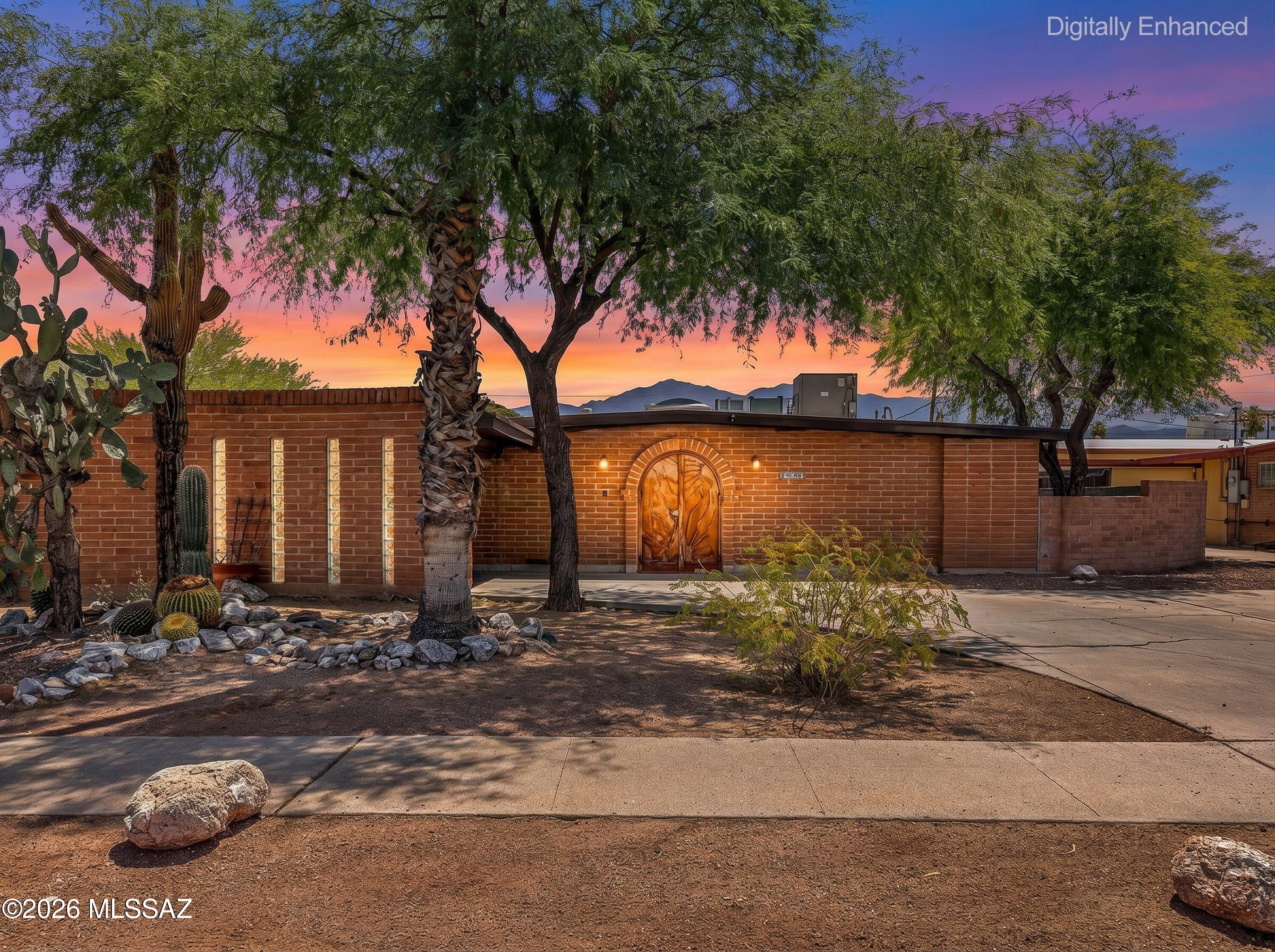 Mid-century brick charmer with a one-of-a-kind personality. The arched entry door with hand-forged desert ironwork sets the tone for a home filled with artisan details: Talavera tile kitchen with skylight, glass-front cabinetry, mosaic foyer inlay, and a soaring stone fireplace anchoring the open living and dining space. Four bedrooms, two baths including an updated primary suite, ceramic tile and vinyl plank flooring throughout. The backyard is built for Tucson living: a freeform pool, expansive covered wood pergola with cafe lights, turf area, and a gated patio zone. Desert-landscaped front yard with mature trees and mountain views at sunset. 1,677 sq ft of character-rich living at an exceptional value.