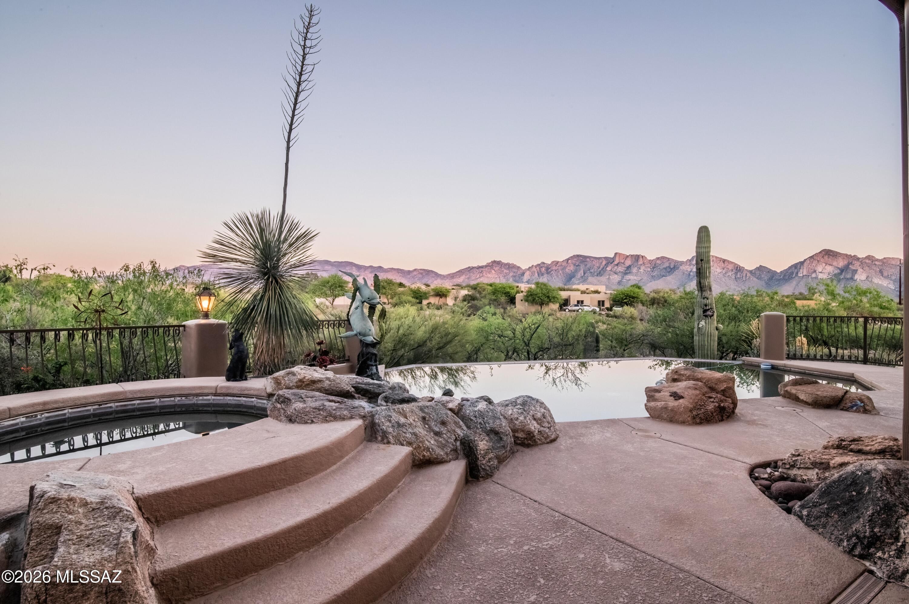 Perched high in the coveted Coyote Ridge enclave of Oro Valley, this extraordinary, gated estate captures the essence of elevated desert luxury. Privately tucked at the end of a cul-de-sac on a premier 1.2-acre ridge-top lot, the home is surrounded by sweeping, unobstructed views of the Catalina Mountains and Pusch Ridge offering a
level of serenity and privacy that is truly rare. Designed for both grand entertainment and refined everyday living, the outdoor experience is nothing short of spectacular. Multiple covered patios with rich wood beams and corbels frame expansive living spaces, while a custom-tiled built-in BBQ, outdoor shower, and a stunning negative-edge Pebble Tec pool with cascading rock waterfall and spa create a true resort-style retreat. From sun-drenched afternoons poolside to unforgettable Arizona sunsets and stargazing evenings, every moment here is elevated. Inside, the home exudes warmth and craftsmanship with wood like tile floors, solid knotty alder doors, and thoughtfully curated finishes throughout. The great room is both inviting and impressive, featuring soaring vaulted ceilings, a striking stacked-stone gas fireplace, and a dramatic wall of windows that perfectly frame the surrounding mountain vistas. The gourmet kitchen is
designed to impress, complete with stainless steel double ovens, a 5-burner gas cooktop, upgraded granite surfaces, custom cabinetry, and a seamless flow into the breakfast bar and dining area, each space thoughtfully positioned to capture
breathtaking views. The primary suite is a true retreat, offering a private sitting area with a dual-sided fireplace, direct patio access, and a spa-inspired bath featuring a jetted soaking tub, oversized tiled shower, executive-height granite vanities, and generous
walk-in closets. An adjoining flex space creates the perfect setting for a private office, fitness room, or relaxation lounge. The quality and attention to detail are evident at every turn in the home with fresh interior and exterior paint plus new plush carpet. The
home is both timeless and impeccably maintained. Backing to expansive preserved open space and offering unmatched privacy, breathtaking views, and exceptional craftsmanship this is a rare opportunity to own one of Oro Valley's most distinctive
luxury properties.