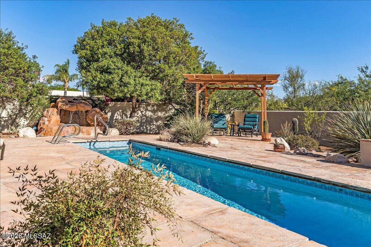 This soft Southwest contemporary home combines generous living spaces, mountain vistas, and mature desert surroundings in a tranquil east side setting.  
Designed for comfortable everyday living with no interior steps, a flexible open plan, and a spectacular yard.
The layout includes three bedrooms, two bathrooms, and a spacious den that could function well as a home office, media room, or play space. Ten-foot ceilings and expansive windows bring in abundant natural light, while neutral finishes and no carpet create a clean, cohesive interior.
At the center of the home, the kitchen features a gas range, quartz countertops, and a breakfast nook positioned to take advantage of the surrounding panoramic mountain views. A large combination living and dining room provides flexibility for entertaining, while the gas fireplace adds warmth and architectural presence to the main gathering space.
The primary suite includes a walk-in closet and a spacious bathroom with dual sinks, vanity area, garden tub, separate shower, and private toilet room. A dedicated laundry room and three-car garage add everyday practicality.
Outdoor spaces are designed for year-round enjoyment, with a screened entry porch, screened rear porch, lap pool, water feature, and mature vegetation creating a private desert setting that balances openness with shade and texture.
With its blend of functional design, natural light, and indoor-outdoor connection, this home offers a relaxed approach to Tucson living in a setting that feels both peaceful and accessible.