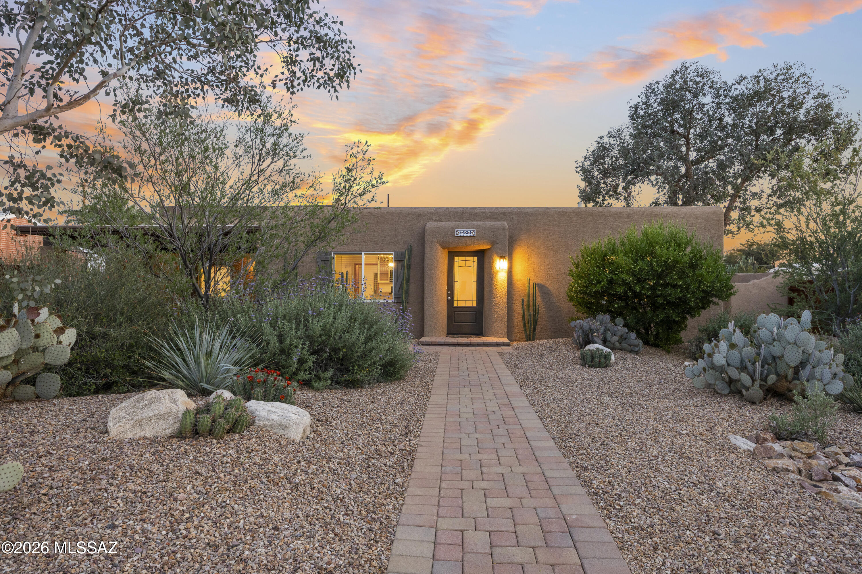 Southwestern Pueblo charm meets modern updates in this renovated La Madera home, freshly painted inside and out, set on a 0.24-acre lot. Windows throughout and skylights in the kitchen and both bathrooms draw natural light into every space. The split floor plan offers two wings, each with its own AC. The kitchen pairs KitchenAid black stainless appliances with a large granite island and white cabinetry accented by reeded glass uppers. The primary bath continues the design with a marble double vanity beneath twin skylights and a glass-enclosed walk-in shower. Outside, a private retreat: professionally designed front and back yards with mature desert plantings, dry creek beds, water harvesting, and drip irrigation. Paver driveway and walkway lead to an attached carport, with privacy walls and mountain views beyond. On a quiet street with direct access to La Madera Park, minutes from U of A, shopping, dining, and the River Walk. Roof with transferable warranty. No HOA.