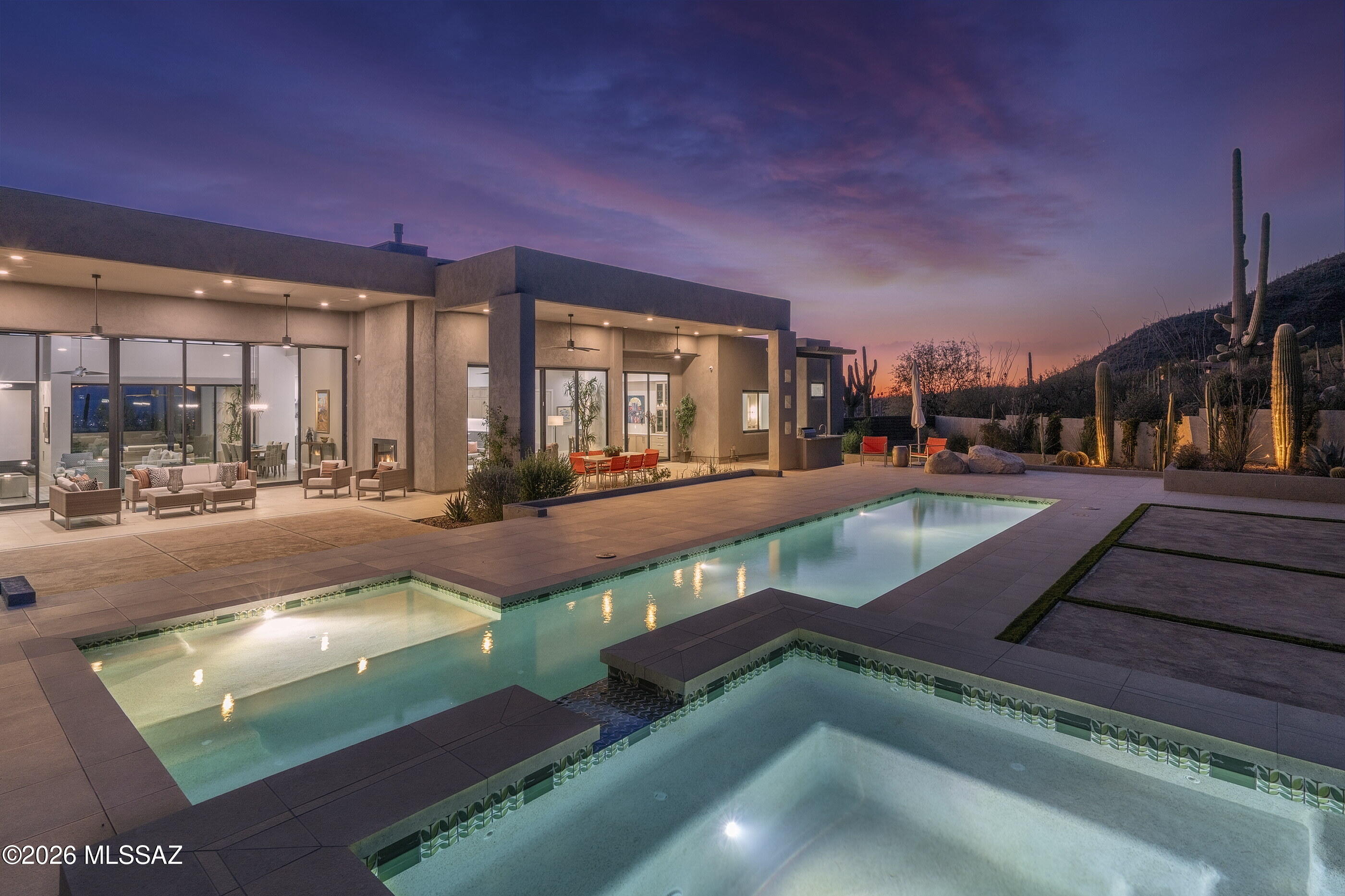 Situated within the prestigious Pima Canyon Estates and secured behind the private secondary gates of Pima Gardens, this exceptional residence exemplifies proportion, restraint, and enduring elegance. Set on one of the most sought after lots within Pima Canyon, this 3.75 acre property offers complete privacy while backing directly to the protected expanse of the Coronado National Forest. Stucco volumes are complemented by stone cladding that anchors the home within its desert setting. Arrival unfolds through a generous motor court, where an oversized 4 bay garage and guest parking establish intentional scale. A gated courtyard entry offers a quiet moment of pause, setting the tone for the seamless transition from exterior to interior. Inside, a soaring foyer introduces the home with measured drama. Emerson Oak oiled hardwood floors paired with large format tile form a cohesive foundation throughout the primary living spaces. North and south exposures draw in soft natural light through expansive Fleetwood glass doors and floor to ceiling walls of glass, framing unobstructed Saguaro studded Catalina Mountain and Pima Canyon views, establishing an immediate connection to the surrounding landscape. As evening falls, southern vistas reveal distant city lights, adding atmosphere to the home's elevated setting.

The formal living room balances refined entertaining with comfort, centered on a striking stone clad fireplace creating a warm focal point. Beyond, informal living areas flow naturally into the kitchen, fostering a harmonious open concept. The kitchen is both a visual centerpiece and high performance workspace, with natural stone countertops finished in Mont Blanc Satin Quartzite defining the kitchen perimeter, waterfall island, breakfast nook, and butlers pantry, paired with custom cabinetry and fully integrated Viking appliances. The media center features a motorized wood paneled roll down that elegantly conceals the articulating television when not in use, preserving the room's design purity while allowing effortless reveal on demand.

The primary suite occupies the eastern wing, designed with bespoke cabinetry, soft natural finishes, and architectural clarity. The primary bath is appointed in Taj Mahal Satin Quartzite, creating a calm, spa-like retreat. Two additional ensuite bedrooms, finished with Ijen Blue Satin Quartzite in select baths, two den/office spaces, and a guest powder room are thoughtfully arranged for privacy and flow. A dedicated dog wash room, designed as a spa retreat for your four legged companions and finished in durable yet refined quartz surfaces, is fully appointed for effortless grooming, ensuring that even the most discerning pooch enjoys a moment of refinement and pampering.

The west wing introduces a fully autonomous guest suite, seamlessly integrated yet completely independent. This private wing features a living room, full kitchen finished with custom millwork and Mont Blanc Satin Quartzite, bedroom, bath, walk-in closet, and dedicated laundry room. Its private patio captures mountain silhouettes and sunset views, ideal for extended stays or multigenerational living.

Indoor and outdoor spaces flow effortlessly, with rooms spilling onto shaded verandas. The backyard extends as an open air living area with clean lines, expansive patios, a resort inspired pool, and spa, all set against the desert landscape. Adjacent, a built-in barbecue and seating area invite relaxed entertaining, framed by a perimeter wall, hardscapes and soft turf accents, allowing the natural surroundings to remain the focus. From this coveted Foothills location, hiking and biking trails, La Paloma Country Club, La Encantada, and the shops and restaurants of Casas Adobes are only moments away, placing the best of Tucson living effortlessly within reach.