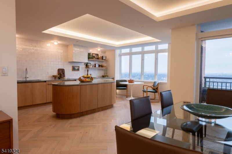 Perched at The Top, SOMA's premier luxury condominium, this fully renovated 3-bedroom residence showcases elevated design, exceptional craftsmanship, and sweeping NYC skyline views. Thoughtfully reimagined with a full designer renovation, every surface and finish has been curated with exceptional taste and attention to detail. An east-facing exposure fills the home with beautiful natural light throughout the day, enhanced by expansive windows and a seamless indoor-outdoor connection to a private balcony. New flooring laid in a sophisticated herringbone pattern, paired with sound-reducing underlayment, adds both style and comfort underfoot. Each of the three spacious bedrooms features its own ensuite full bath. The primary suite features a dressing area and bath with a soaking tub, stall shower w/new glass door, and refined new tile work. A stylish powder room off the hallway is ideal for guests, while custom built-in closets throughout provide exceptional storage solutions. The showstopping kitchen features custom wood cabinetry, marble counters, open shelving, and new appliances. A striking rounded center island anchors the space. Thoughtfully selected light fixtures and cove lighting on dimmers create the perfect ambiance throughout. Boasting one of the largest floorplans in The Top at 2500+ sqft, this home offers refined suburban living in the vibrant heart of Essex County, just moments from everything South Orange and Maplewood have to offer.