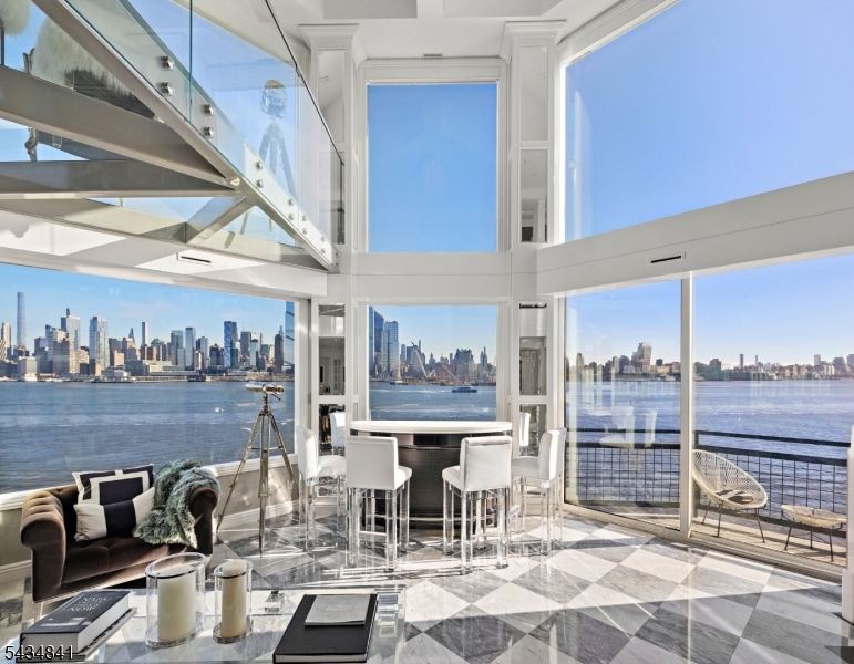 Stunningly unique 2-story penthouse in the sky with breathtaking panoramic NYC & Hudson River views! Step off your private elevator to see gorgeous south NYC views and a custom glass staircase with built-in wine storage. Walk into the heart of the home and be surrounded by the entire NYC skyline: this 2-story great room has a bar, custom fireplace, and balcony, while allowing you to see all the way from the George Washington Bridge to the Verrazano Bridge. Turn around and you're in your spacious chef's kitchen with white cabinetry and countertops, custom sink with instant hot water, oversized island and LaCornue stove with 8 burners and a pot filler.  The dining area has incredible northern views and its own balcony. The living room has custom paneling and storage, a wet bar with a dishwasher and freezer, and an additional balcony with stunning views. The upstairs landing is a luxurious custom office space with built-in shelves and a mirrored wall (with a hidden TV) to reflect the incredible views.  The expansive primary suite has an attached glass loft over the great room, panoramic views, skylights, a fireplace, walk-in closet, and a enormous ensuite bathroom with its own views over dual sinks, an enormous soaking tub, and walk-in shower with four showerheads. This home was completely redone with private storage and 2 garage parking spaces. Riva Pointe offers 24/7 concierge and security, an indoor pool, fitness center, sauna, sundecks, and landscaped terraces.