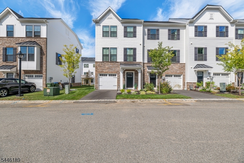 Built in 2024, loaded with premium upgrades, this stunning three-story end-unit townhome blends modern luxury, comfort, and convenience. From the moment you enter, you're welcomed by wide-plank wood flooring, neutral designer paint, soaring ceilings, recessed lighting, and custom window treatments that create a bright, sophisticated ambiance throughout. The 1st level offers a gracious foyer, convenient powder room, and a spacious open family room with sliding doors leading to a patio perfect for relaxing. Upstairs, the sun-filled main living level showcases an impressive custom kitchen designed to be the heart of the home. Crisp white cabinetry, a grand center island with built-in breakfast bar, and elegant pendant lighting make the space both stylish and functional. The kitchen flows seamlessly into the dining and living areas, creating an expansive open-concept layout ideal for gatherings. Large windows flood the home with natural light, while an elevated wooden deck extends your entertaining space outdoors. The 3rd floor features three generously sized bedrooms and two full baths. The luxurious primary suite includes a tray ceiling with recessed lighting, a spacious walk-in closet, and a private ensuite bath with dual vanity. A well-appointed hall bath with tub and shower serves the additional bedrooms. Immaculate and move-in ready, this exceptional home is just moments from the center of Hackettstown, with its charming shops, restaurants, and NJ Transit service to NYC.