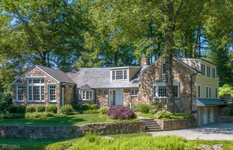 Set atop Bernardsville Mountain on approximately 8 private acres, this exceptional property offers timeless charm, sophisticated country living, and convenient access to New York City. A crushed-stone drive crosses a picturesque fieldstone bridge over a flowing stream before arriving at a beautifully restored and expanded stone residence surrounded by mature trees, flowering gardens, a spring-fed pond, and expansive bluestone terraces. Renovated and expanded in 2015, the home features a slate roof, a stunning great room with vaulted ceilings, exposed beams, radiant heated floors, designer lighting, and walls of glass. The designer kitchen showcases custom Amish cabinetry, two oversized islands, premium appliances, and built-in banquette seating. The first floor includes a lovely primary bedroom and a separate ensuite guest bedroom, while the second level offers three additional bedrooms and two updated baths. A charming 5 room, 1 bedroom guest cottage (kitchen and bathroom updated in 2025) detached oversize 4-car garage, barn, whole-house generators for main residence and cottage, and Sonos system in main house complete this rare offering. Fireplaces are "as is" no known issues. Barn "as is"