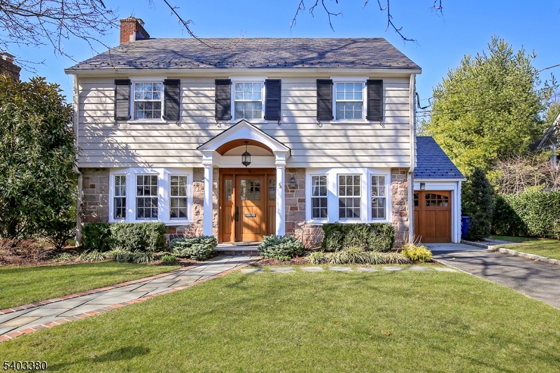 Excellent curb appeal and prime location define this stone and clapboard Colonial, just blocks from downtown Summit, the train station, and top-rated schools including Lincoln-Hubbard. A slate roof, carriage-style garage, brick paver walkways, and mature professional landscaping enhance the exterior, while a classic center hall layout sets the interior tone. Sunlight pours through bay windows into the open living and family rooms, anchored by a gas-log fireplace and offering front-to-back views. The formal dining room features raised paneling and a ceiling medallion, ideal for entertaining. The updated designer kitchen showcases white cabinetry, black granite countertops, a dark wood island, and radiant heated tile floors that extend into the powder room. A breakfast-area door opens to a private bluestone patio with decorative lattice fencing. The second floor offers four well-appointed bedrooms with custom closets and a spacious primary suite with hardwood floors, custom double closet, Hunter Douglas window treatments, and a bath with claw-foot tub and frameless glass shower. A generous hall bath completes the level. A private fifth bedroom with renovated bath and attic storage occupies the third floor. Renovated lower level provides flexible living space with recreation area, home gym, office, laundry room, and pantry/storage. The private, level yard is ideal for outdoor dining with a built-in grill and patio. A true Summit gem in a sought-after neighborhood.