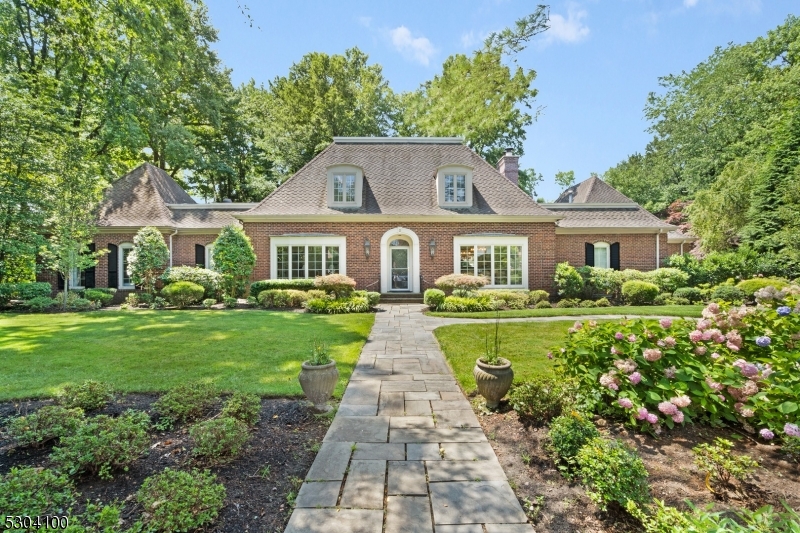 Discover this elegant French Country brick estate, nestled in the coveted Holmehill Section of Roseland, just 22 miles from New York City. In close proximity to five great country clubs. Luxury and tranquility greets you as you drive up the private driveway to the three-car garage. Step inside to a grand foyer, where custom moldings and rich oak flooring set the stage for a home of exceptional detail. The first-floor primary bedroom offers a private retreat with a full bathroom, adding convenience. The stately family room serves as a centerpiece of the home, featuring a floor-to-ceiling brick fireplace, a custom built-in wall unit, and a well-appointed wet bar. The chef's kitchen is stylish, boasting granite countertops, stainless steel appliances, a Wolf cooktop, dual ovens, and a generously sized peninsula with seating. From here, enjoy seamless access to the rear terrace, overlooking a beautifully landscaped yard with European-inspired gardens. Upstairs, you'll find three generously sized bedrooms, full bath with steam shower, and a walk-up attic with cedar-lined storage. Basement is finished &  furnished. Above the garage, a private in-law suite with its own bath and walk-in closet offers an ideal space for guests. House has propane generator. The backyard has a stunning gunite concrete pool, a blue stone patio, and a spa. A poolside cabana with a full bath adds an extra layer of convenience, making this home the ultimate retreat for elevated living.