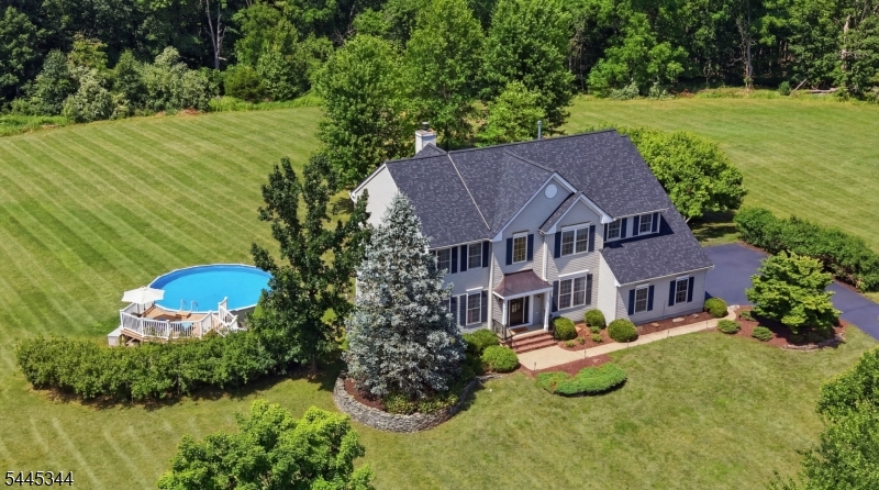 Located in the sought-after Estates at West Amwell community, this beautifully maintained four-bedroom, 2.1-bath home offers spacious living, and a private setting just minutes from Lambertville, New Hope, and everyday conveniences. A freshly sealed driveway, attractive landscaping, and inviting curb appeal create a wonderful first impression. Inside, a dramatic two-story foyer features tile flooring, detailed millwork, and a turned staircase with wrought iron balusters. Hardwood flooring extends throughout much of the main level. The floor plan includes formal living and dining rooms, a private office/library, and a first-floor laundry room. The spacious eat-in kitchen overlooks the backyard and opens to the family room and outdoor living spaces. The two-story family room is filled with natural light from oversized arched windows and skylights and features a wood-burning fireplace. Upstairs, the primary suite offers two walk-in closets and an updated bath with dual sinks, a soaking tub, and glass-enclosed shower. Three additional bedrooms share a hall bath, while the open hallway overlooks the family room below. The finished walk-out lower level offers recreation space, a home gym area, and a dry sauna. Sliding doors lead to a covered patio and hot tub. Outdoor living includes a spacious deck with two staircases to the level, tree-framed backyard, plus an above-ground pool with surrounding deck space. Additional highlights include a two-car garage and roof replaced in 2024.