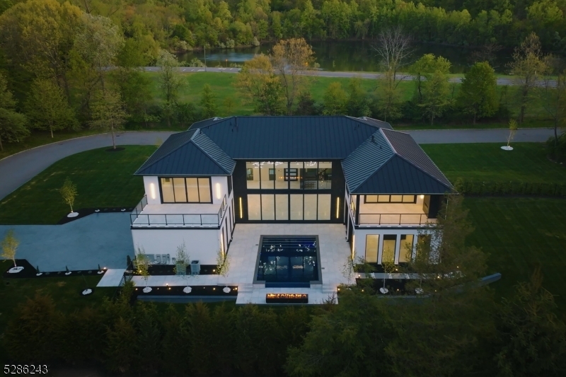 This architectural gem featuring 5 bedrooms, 7 full and 1 half bath radiates modern elegance. Its grand entrance showcases a stunning pivot door, revealing a light-filled foyer with towering windows. The two-story great room boasts panoramic views and flows into a state-of-the-art kitchen. A highlight of this home is a 3-story floating staircase crowned with a 28-foot chandelier. The property features a luxurious primary suite that offers unparalleled privacy, a spa-like bathroom, spacious walk-in, and a private balcony. The second floor features four additional luxe ensuite bedrooms. Outside is a custom pool backed by a fire pit lounge.