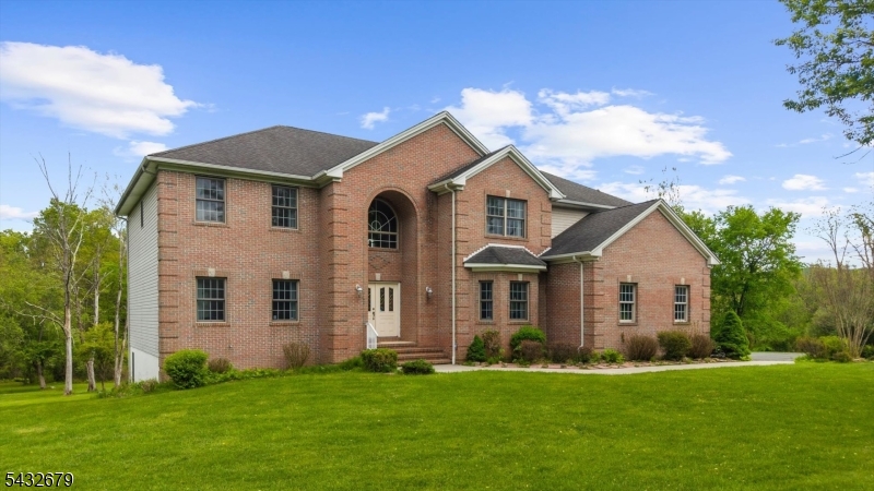 Tucked down a long private driveway on 7.65 acres in Union Township, this colonial sits where Hunterdon County gives you space to actually breathe. Oversized windows pull natural light through the interior, hardwood floors run through most of the main level, and the two-story foyer sets a tone that feels open and grounded at the same time. Rooms flow into one another without losing their purpose, which is harder to find than it sounds. The kitchen is where everyone ends up, with generous counter space, solid cabinet storage, and a door that opens straight out to the deck overlooking the property. The separate living and dining rooms with tray ceilings handle whatever the season calls for, whether that is a gathering or a quieter night in. The family room earns its keep with soaring ceilings, a gas fireplace, and a rear staircase that keeps traffic moving naturally through the home. A main floor bedroom with a full bath nearby covers a home office or guests without any awkward workarounds. Upstairs, four well sized bedrooms each have their own bathroom access. The primary suite is tucked away from the rest, with custom walk-in closets, a sitting room, and an enormously sized bath. The home also runs efficiently. A hybrid HVAC system and solar energy credits completely offset the electric bills, which is the kind of detail that matters more every year. Close to 78 and all of Clinton's amenities, but once you are down that driveway, it feels like a world of its own.